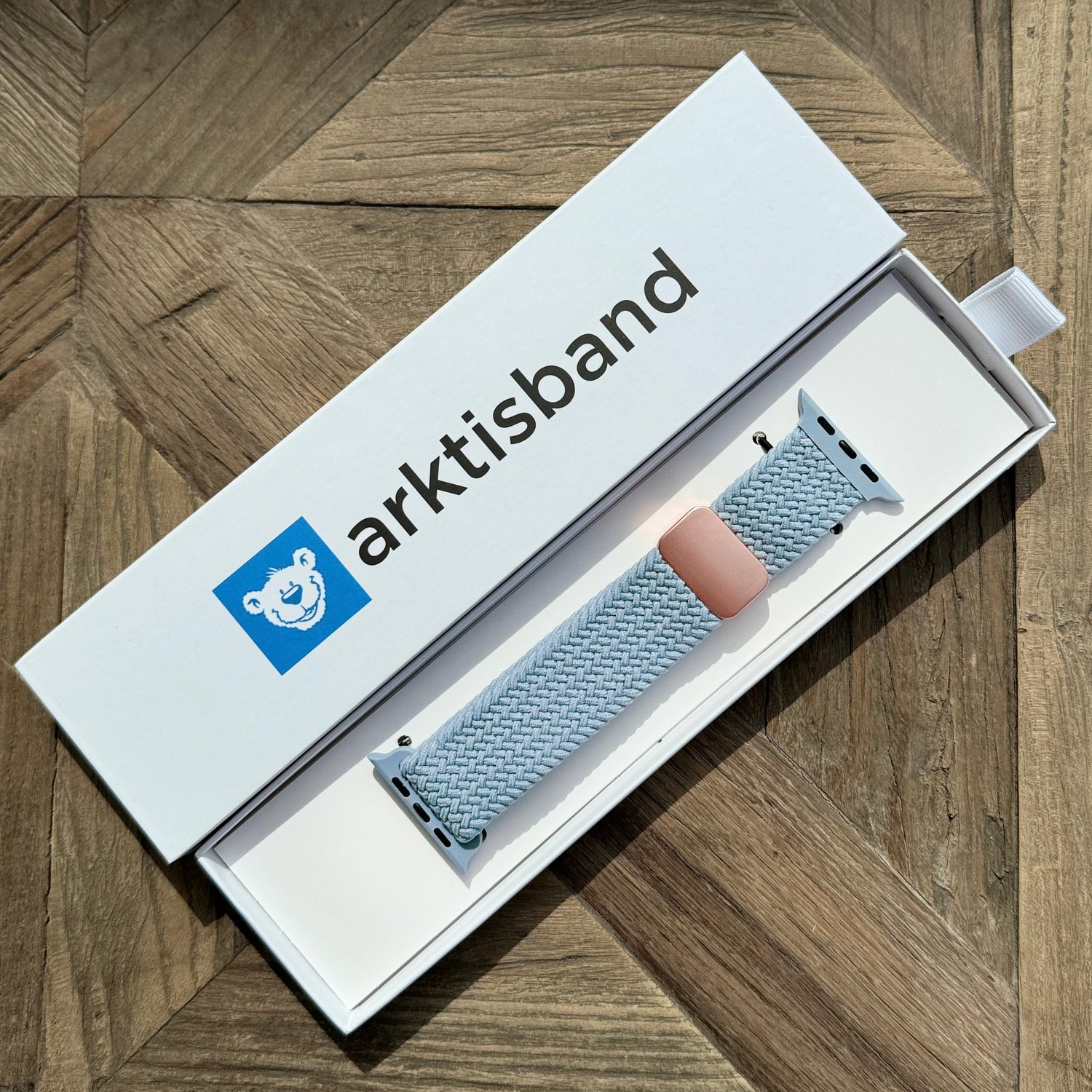 Das kunstvoll geflochtene Apple Watch Armband „Casual“ mit Magnetverschluss in Blau liegt in einer offenen weißen Box auf einer Holzoberfläche.