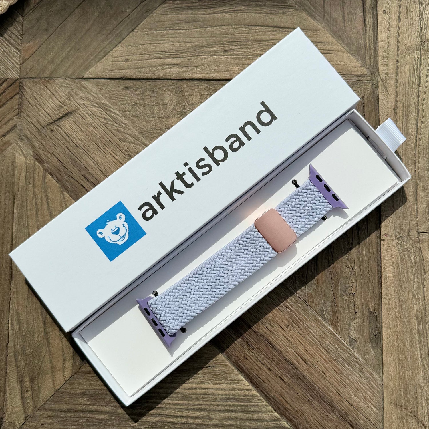 Das arktisband Geflochtene Apple Watch Armband „Casual“ mit Magnetverschluss von arktisband liegt in einer weißen Box auf einer Holzoberfläche.