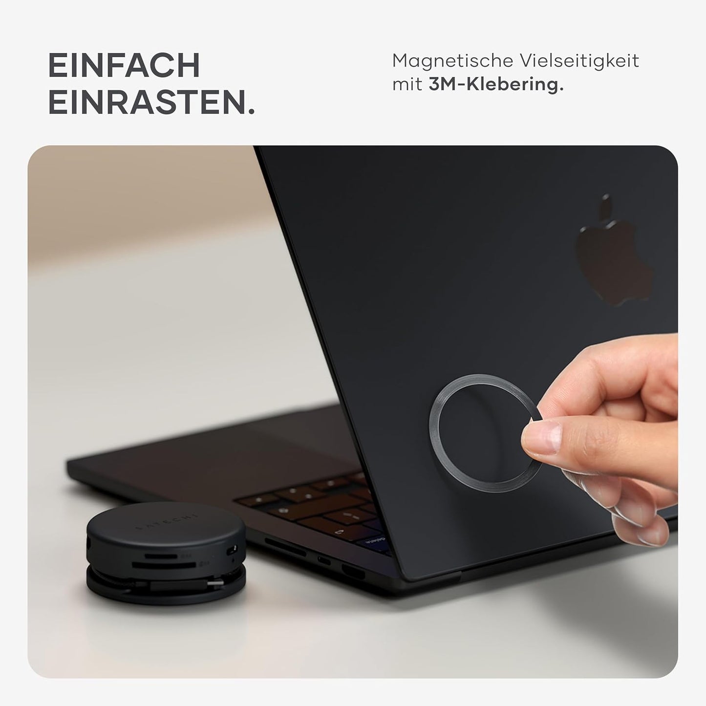 Eine Hand bringt einen magnetischen Ring an einem schwarzen Laptop an und unterstreicht damit die Vielseitigkeit des Satechi OntheGo 7-in-1 Multiport-Adapters. Der deutsche Text beschreibt, wie der starke 3M-Kleber Ihren Satechi USB-C Hub für mehrere Anwendungen sichert.