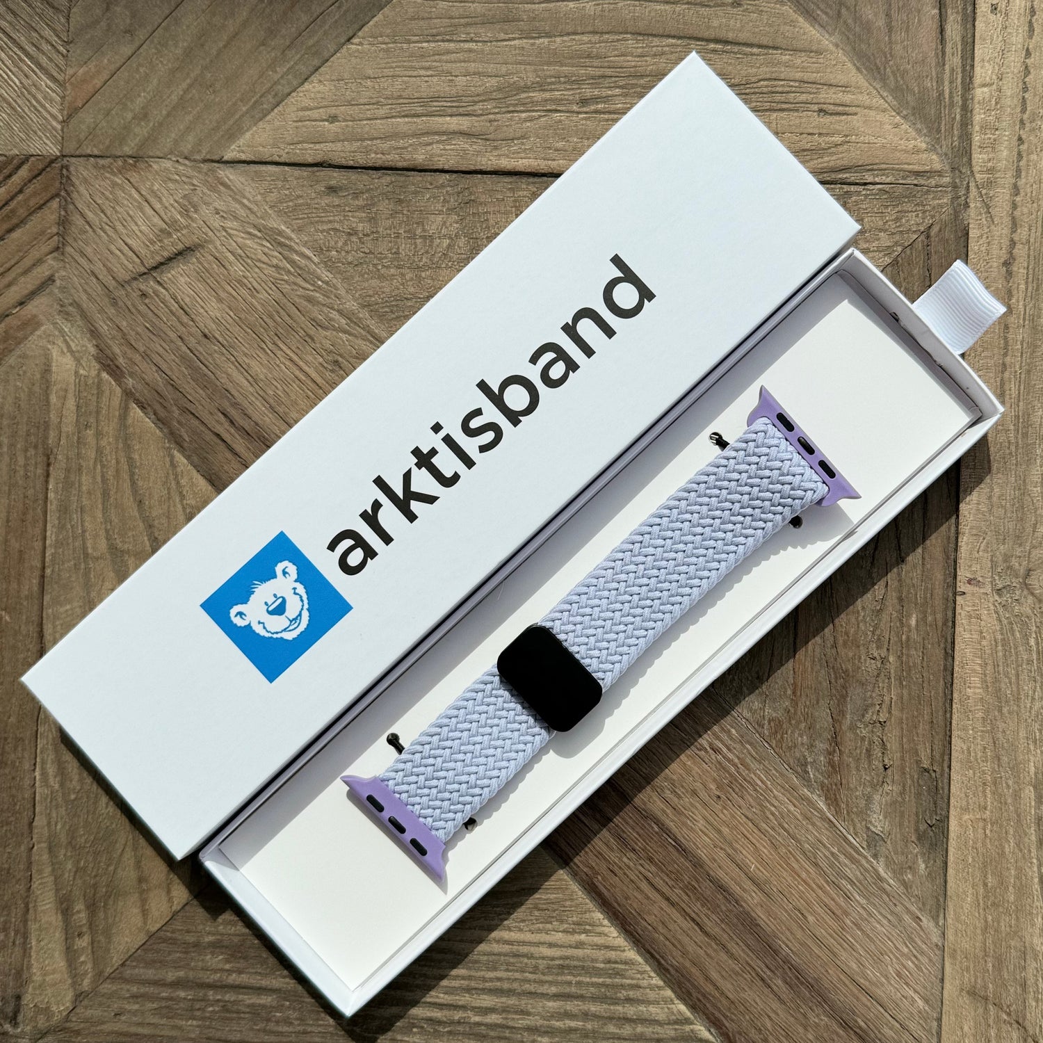 Das arktisband Geflochtene Apple Watch Armband „Casual“ mit Magnetverschluss wird in der weißen arktisband Box auf einer Holzoberfläche präsentiert.