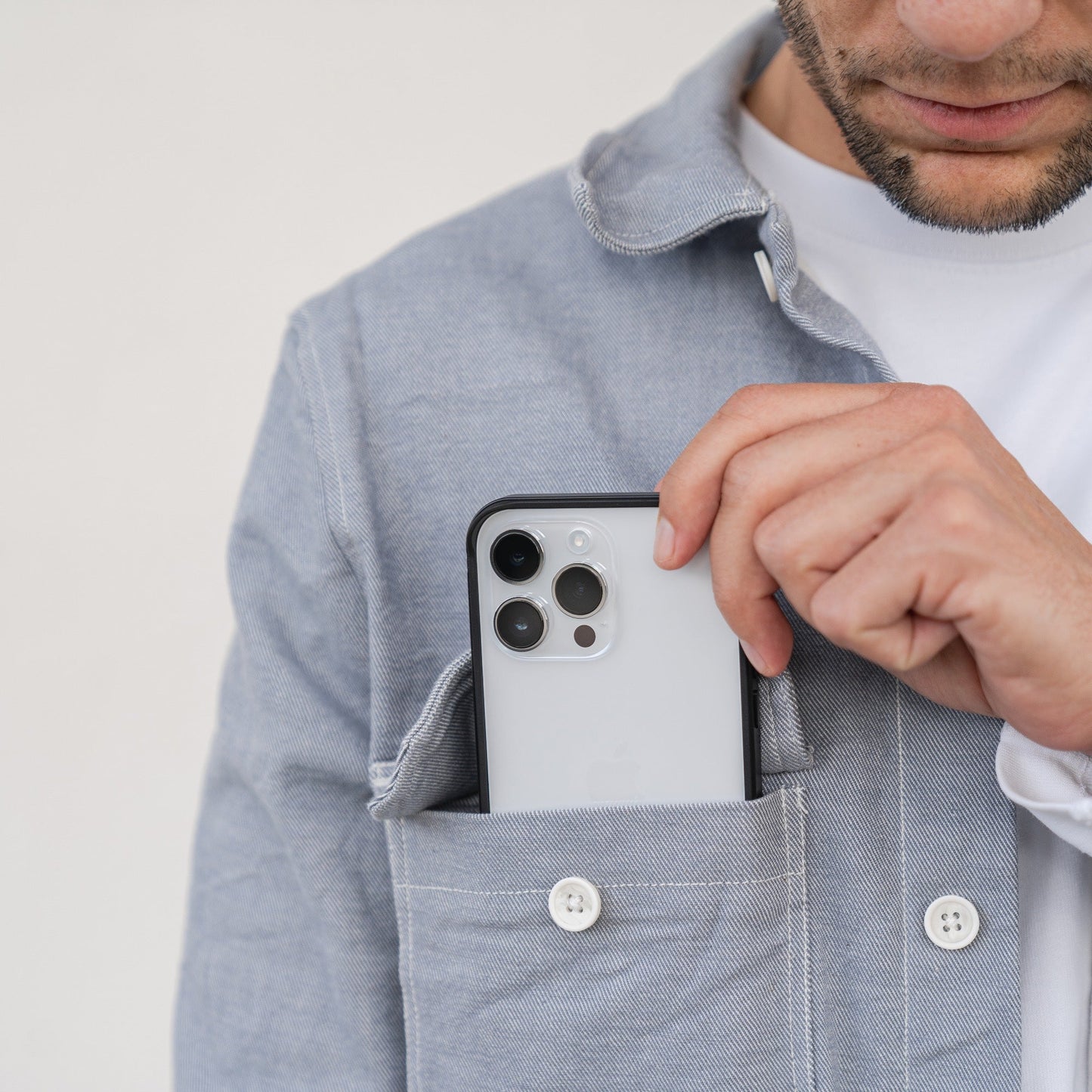 Ein Mann steckt ein Smartphone mit dem aus Flugzeugaluminium gefertigten Aviato AirZERO Alu Bumper für iPhone 15 Pro Max von Aviato in die Brusttasche eines hellgrauen Hemdes.