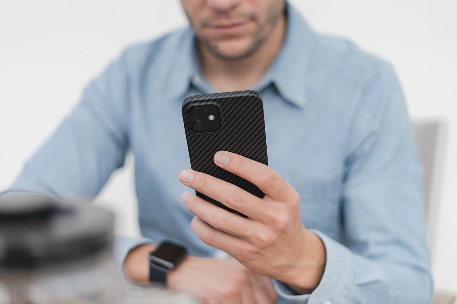 Mann in einem blauen Hemd, der ein Smartphone hält und auf den Bildschirm schaut, an einem Tisch sitzend.