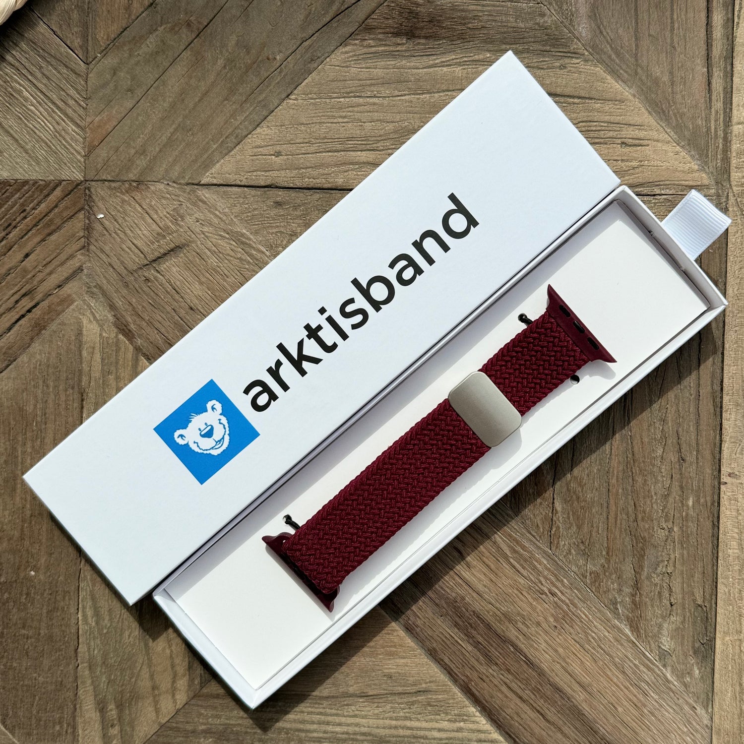 Das arktisband Geflochtene Apple Watch Armband „Casual“ mit Magnetverschluss in Rot, stilvoll präsentiert in einer weißen arktisband Box auf einer Holzoberfläche.