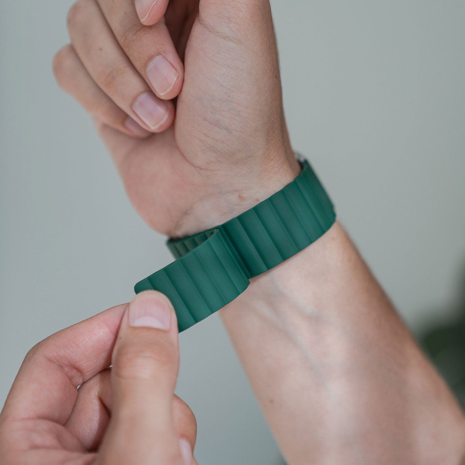 Eine Person befestigt ein grünes geripptes Uhrenarmband um ihr Handgelenk.