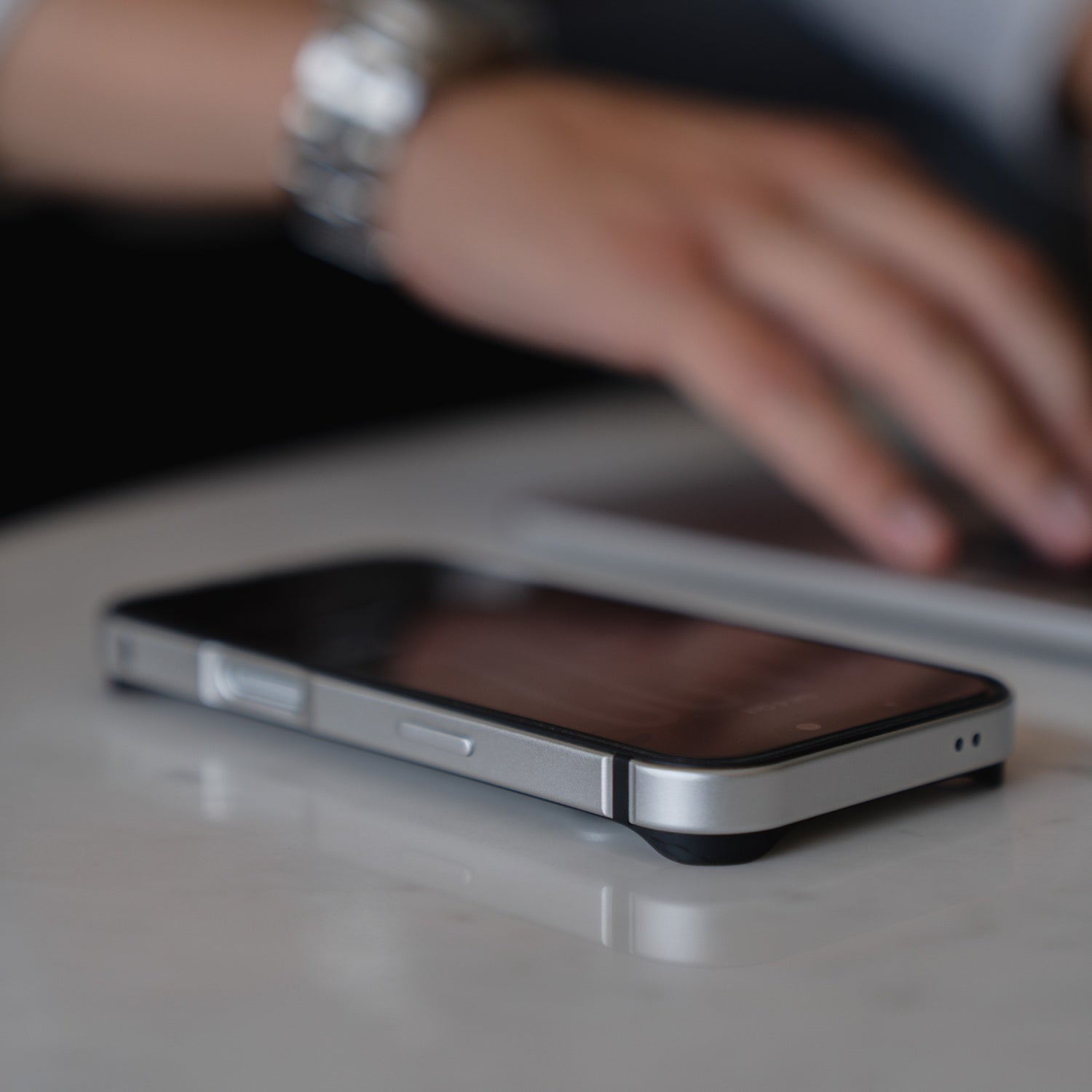 Ein Smartphone mit dem arktis iPhone 17 Pro Bumper liegt auf dem Tisch, während im Hintergrund eine Hand auf einem Laptop tippt.