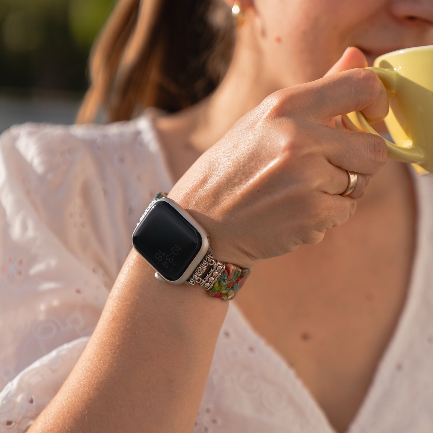 Eine Frau in einem weißen Oberteil trägt ein Arktisband Apple Watch „Stone Loop“-Armband und hält eine gelbe Tasse nah an ihren Mund.