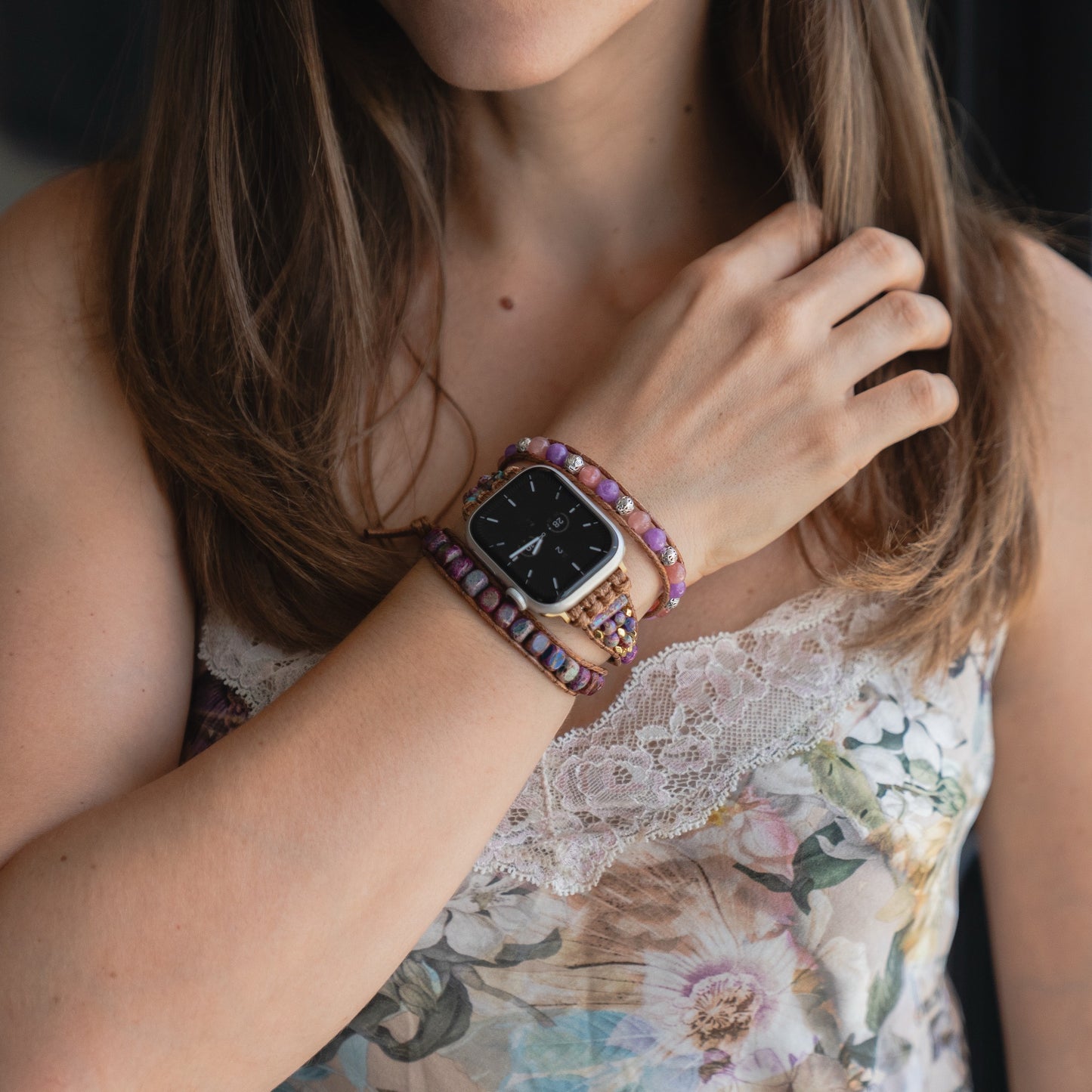 Eine Frau trägt ein geblümtes Oberteil, das arktisband Apple Watch Armband "Dream Catcher" von arktisband mit Edelstahladapter und lila Perlenarmbänder im Boho-Stil an ihrem Handgelenk.