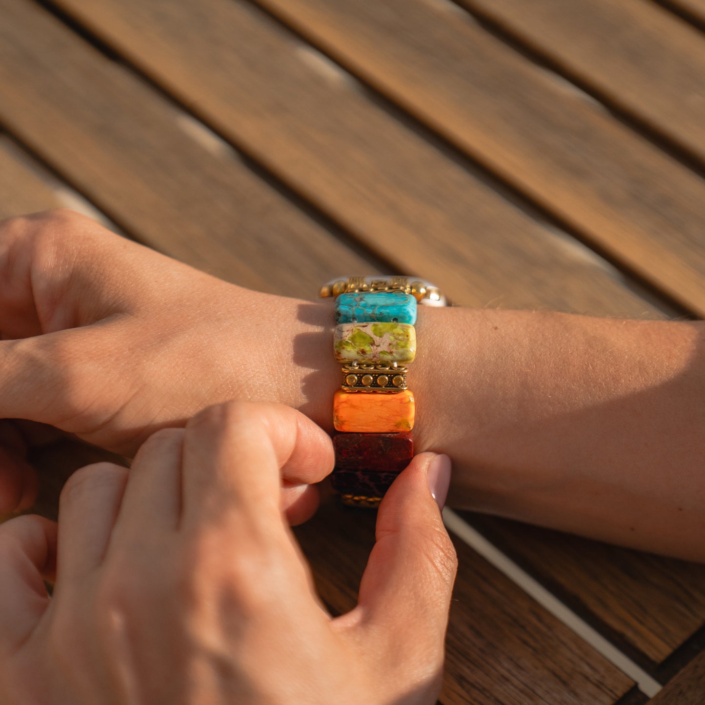 Eine Hand passt die farbenfrohe arktisband Apple Watch „Stone Loop“ von arktisband an einem Handgelenk über einem Holztisch an – ideal als stylisches Armband oder in Kombination mit Ihrer Apple Watch.