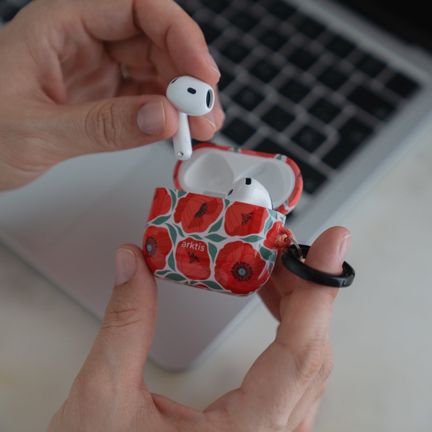 Hände, die eine geöffnete Arktis AirPods 5-Hülle halten – das kabellose Etui Summer Garden mit rotem Mohnblumenmuster.