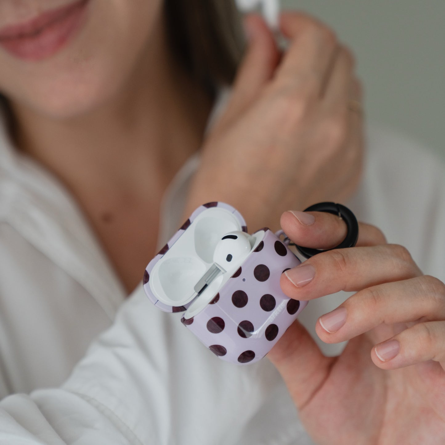 Eine Person, die eine violette, mit weißen Punkten verzierte Arktis AirPods 5-Hülle – Sweetie – in der Hand hält, in der sich ein Ohrhörer befindet.