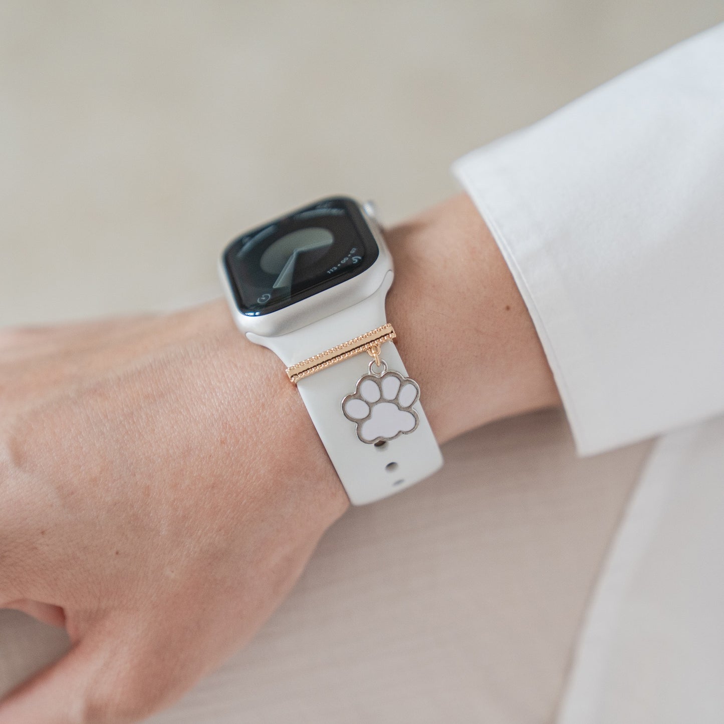 Eine Person trägt eine weiße Apple Watch mit arktisband Apple Watch Armband Charms im goldenen und silbernen Pfotendesign, gepaart mit einem weißen Langarmshirt – ein exklusives Accessoire von arktisband für individuelle Gestaltung.