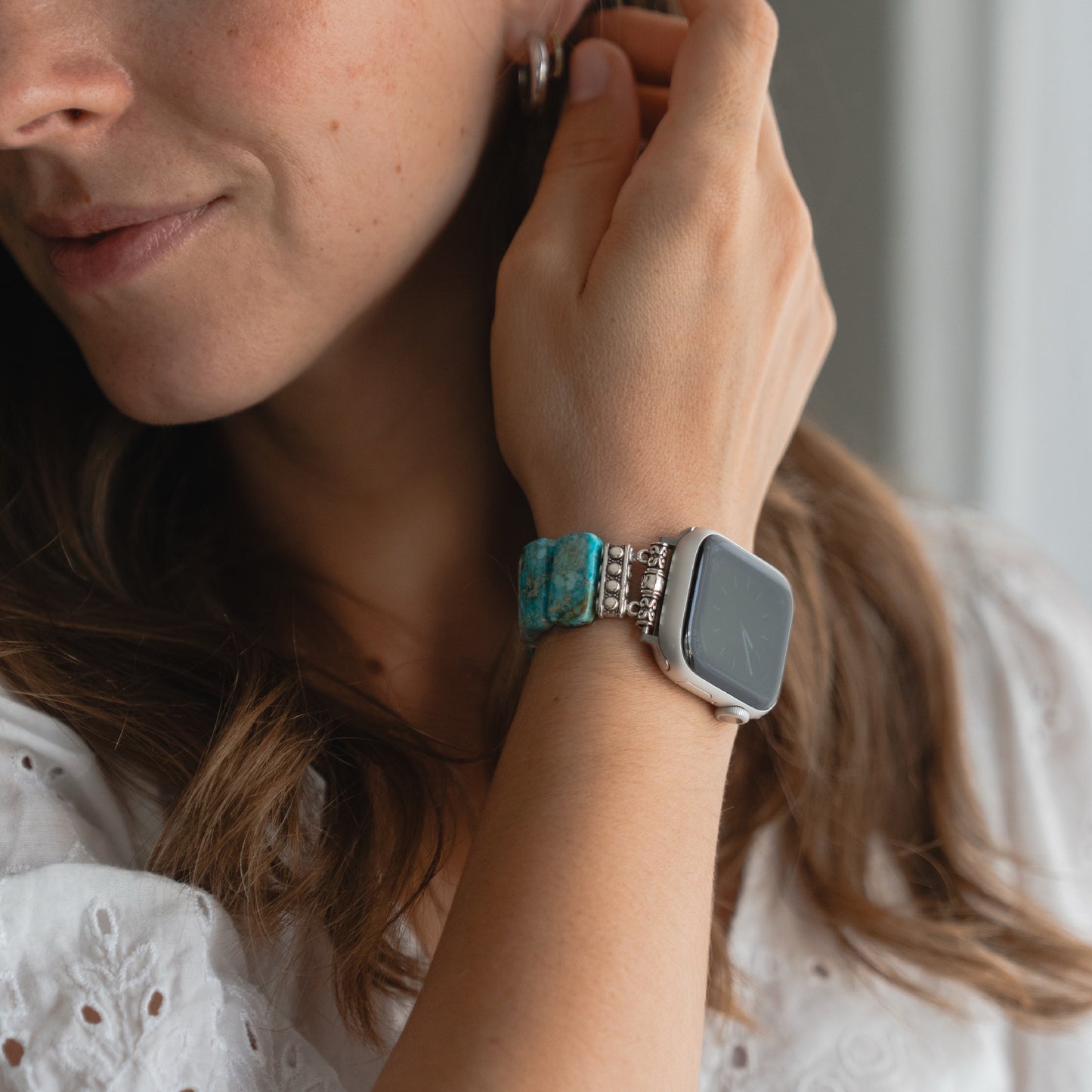 Eine Frau trägt die arktisband Apple Watch "Stone Loop", ein türkisfarbenes Natursteinband von arktisband, mit der Hand am Ohr.