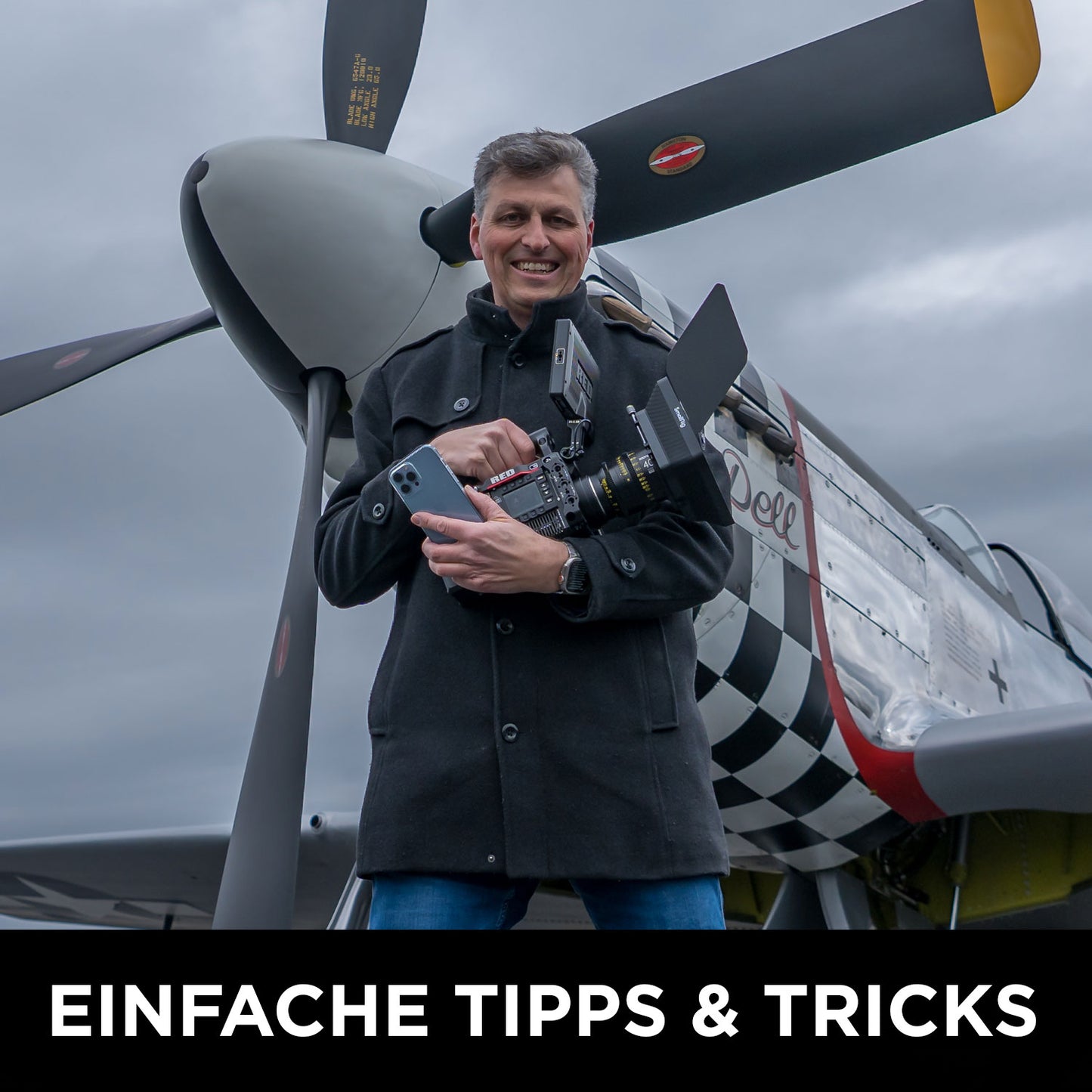 Ein Mann in einem dunklen Mantel steht vor einem Oldtimer-Propellerflugzeug und hält eine professionelle Videokamera unter bewölktem Himmel. Text: EINFACHE TIPPS & TRICKS – entdecke den Rainer Wolf Wolffilms Academy Online-Kurs – Einfach filmen lernen.