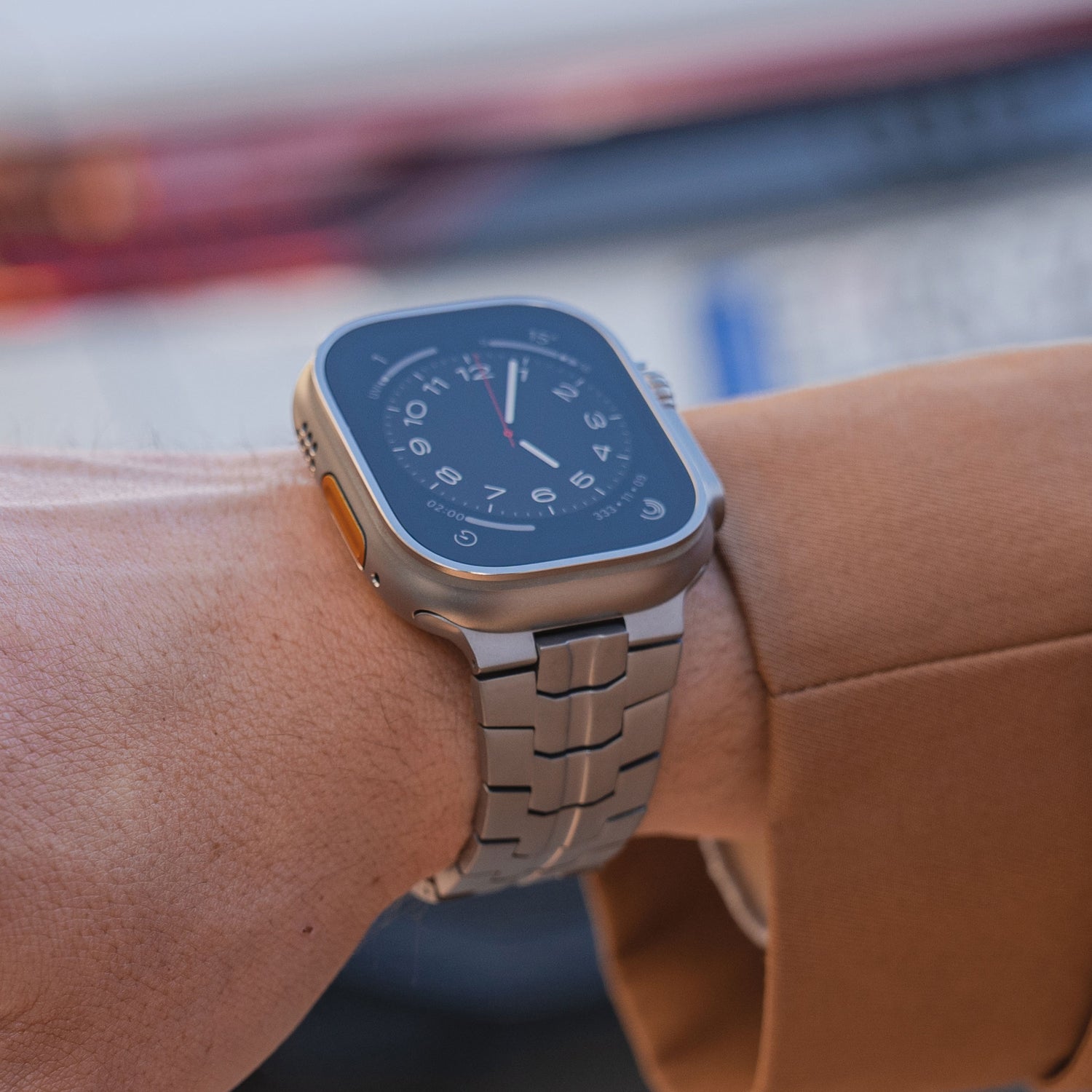 Eine Person trägt eine silberne Smartwatch mit Metallarmband und schwarzem Zifferblatt und ist mit einer braunen Jacke bekleidet.