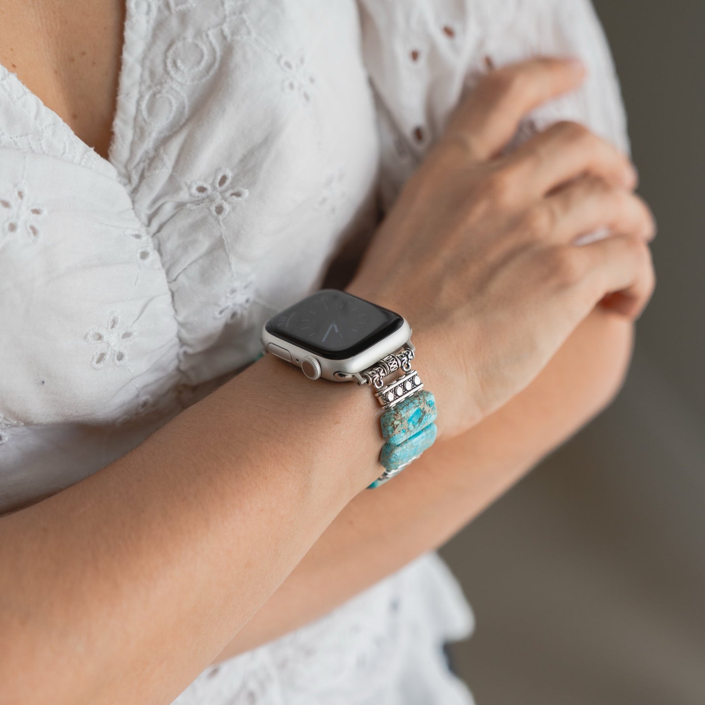 Eine Frau trägt eine weiße Bluse und die arktisband Apple Watch "Stone Loop" von arktisband mit türkisfarbenen und silbernen Steinen für einen eleganten Look.