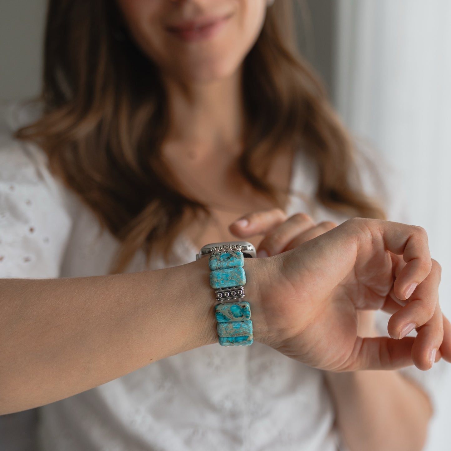 Eine Frau, die eine arktisband Apple Watch "Stone Loop" von arktisband in Türkis trägt, lächelt, während sie diese an ihrem Handgelenk präsentiert.