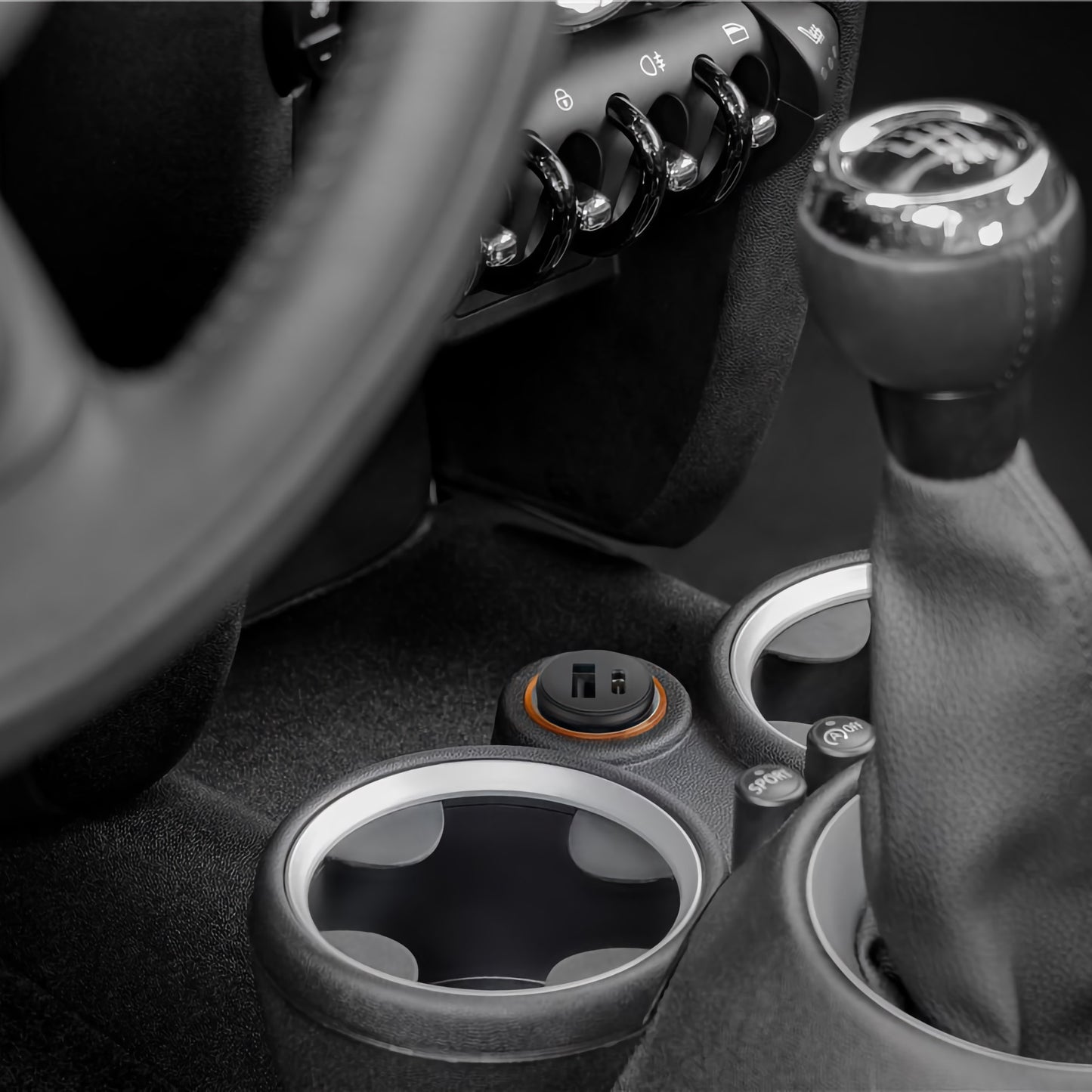 Nahaufnahme der Mittelkonsole eines Autos mit Getränkehaltern, manueller Gangschaltung und einem Goobay Dual USB Auto-Schnellladegerät USB-C PD 45 W mit Schnellladefunktion.