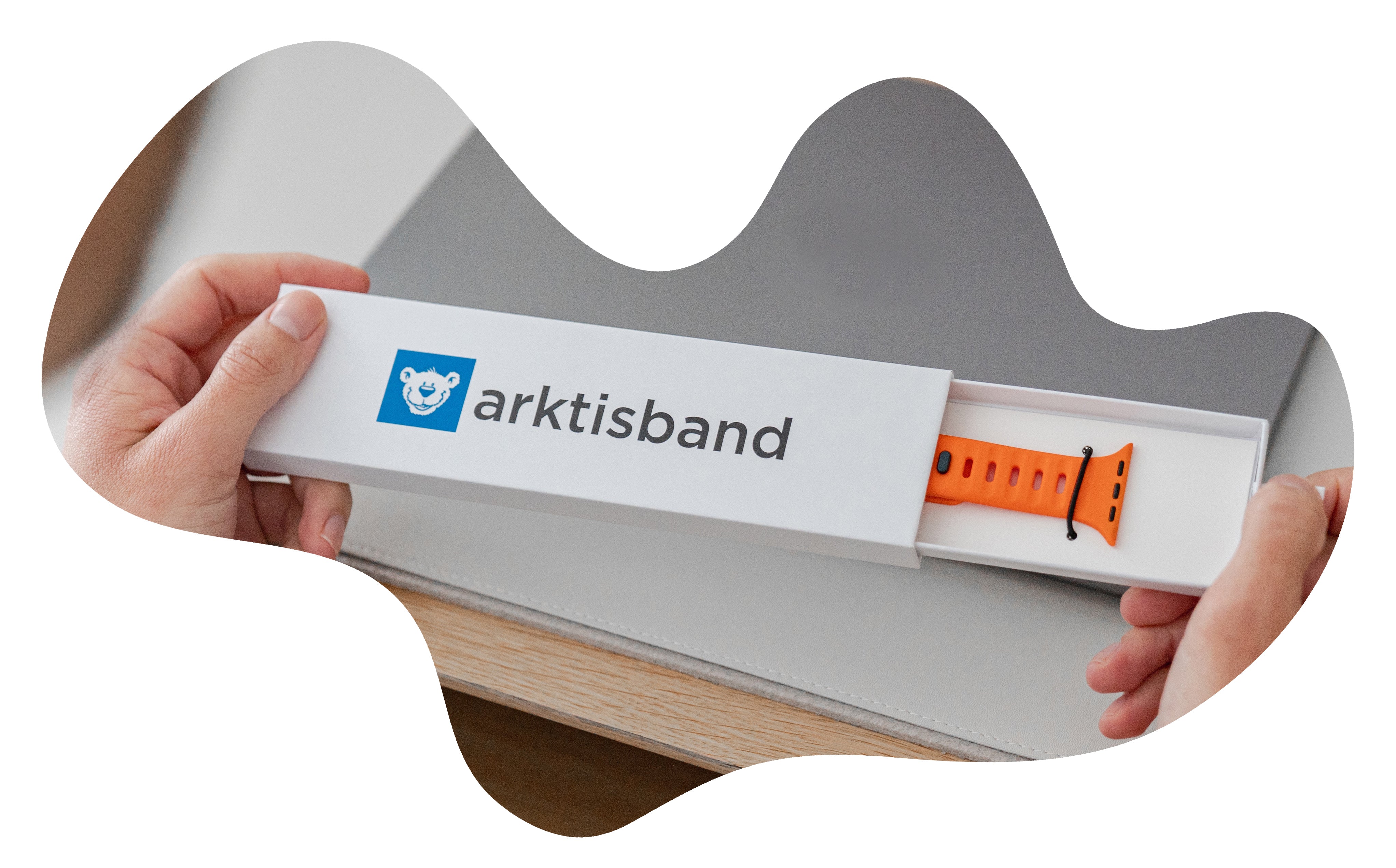 Hände öffnen eine Arktisband-Box mit einem orangefarbenen Smartwatch-Armband darin.