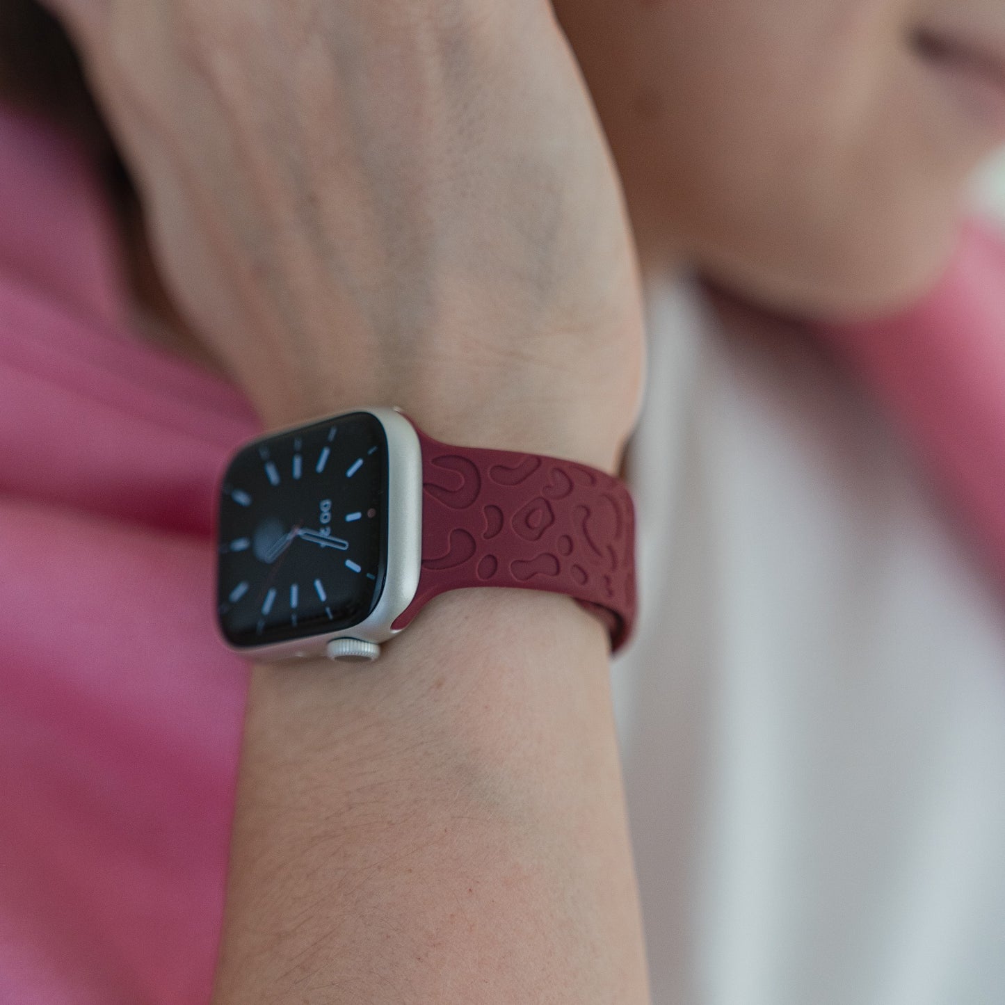 Eine Person mit einem rosa Kleidungsstück über der Schulter trägt das arktisband Apple Watch Armband „Leopard“ am Handgelenk und zeigt auf ihrer Smartwatch 9:00 Uhr an.