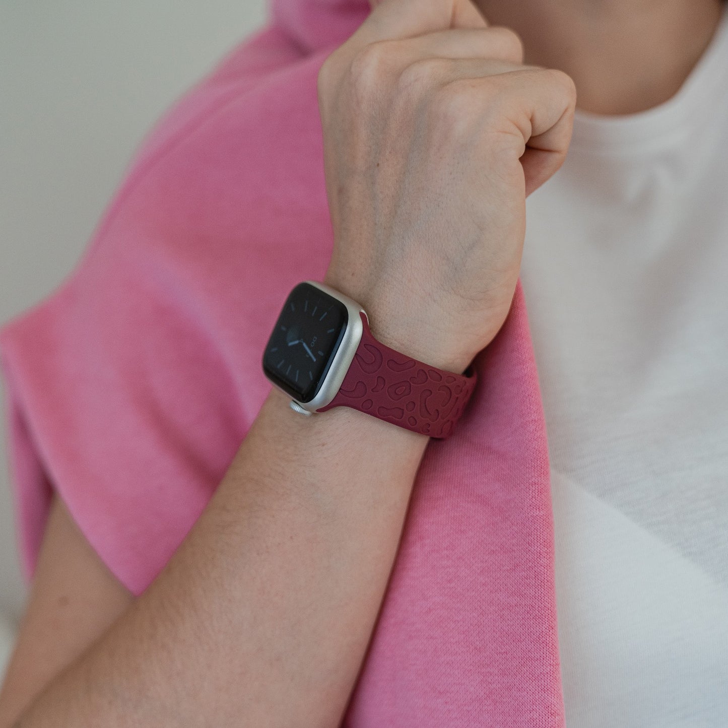 Eine Person mit einem rosa Pullover über den Schultern hält den Kragen eines weißen Hemdes und trägt dabei das arktisband Apple Watch Armband „Leopard“ von arktisband, das die Uhrzeit anzeigt und mit der Apple Watch kompatibel ist.