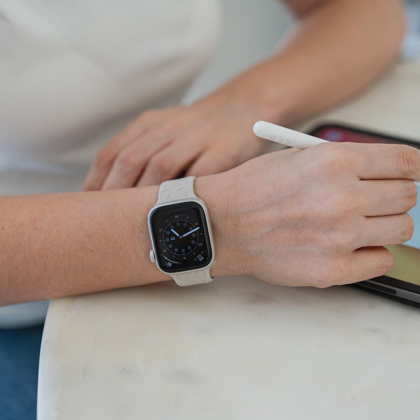 Eine Person trägt das arktisband Apple Watch Armband "Leopard" mit Silikonarmband, hält einen Stift und bedient ein Tablet auf einer Marmoroberfläche. Die Apple Watch-kompatible Smartwatch zeigt ein analoges Zifferblatt.