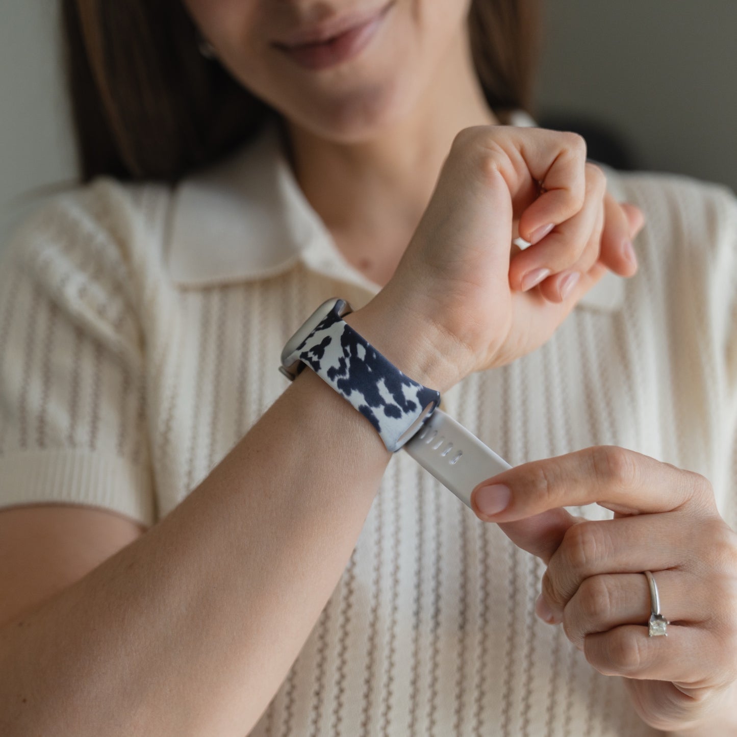 Eine Frau in einem weißen Hemd richtet ihr „Arktisband Kuhfell Apple Watch“-Armband von arktisband mit gemustertem Band an ihrem Handgelenk zurecht.