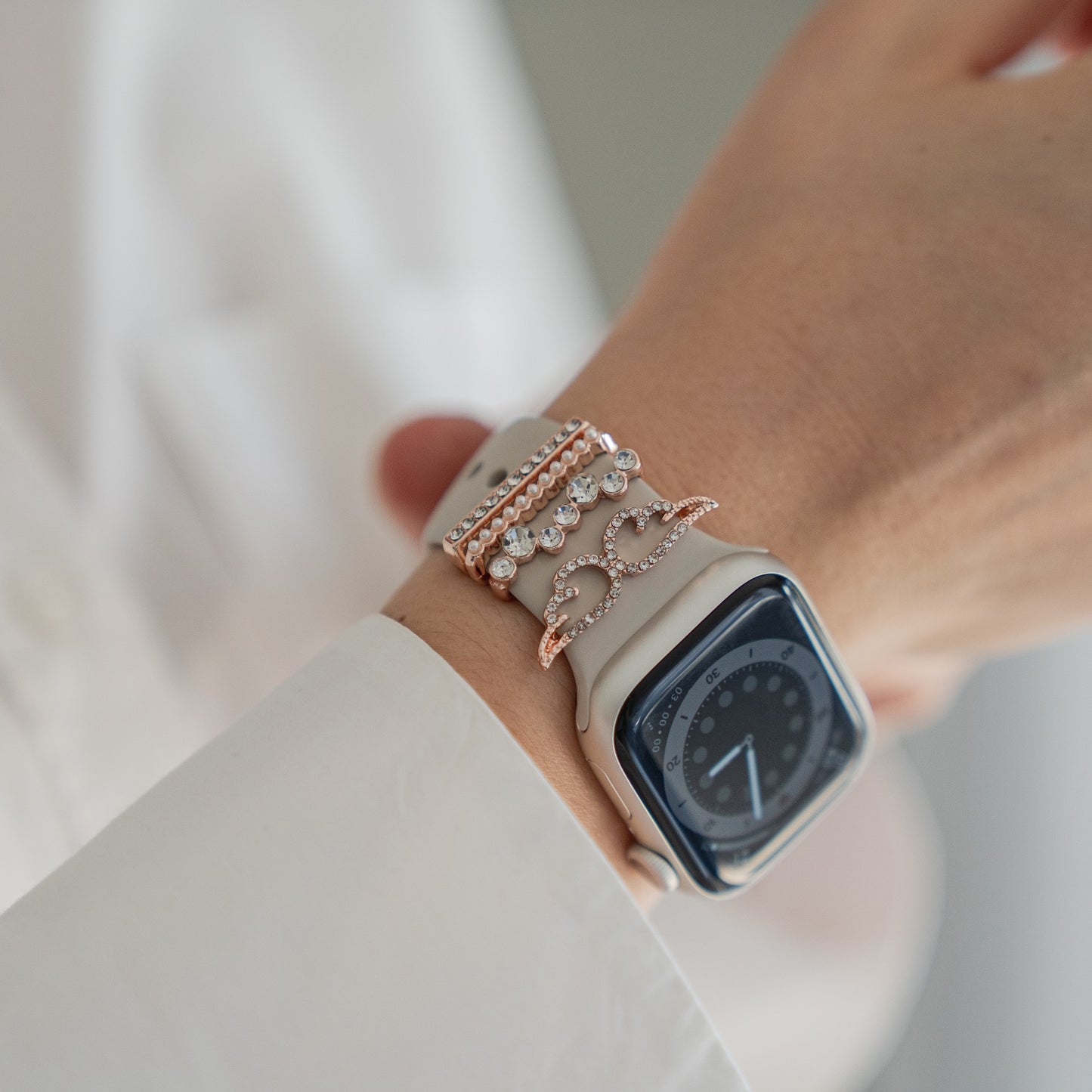 Eine Person in einem weißen Langarmhemd trägt eine Smartwatch mit einem Arktisband und drei Metallarmbändern, die jeweils mit Arktisband-Apple-Watch-Armband-Charms verziert sind, um ihren Stil individuell zu personalisieren.