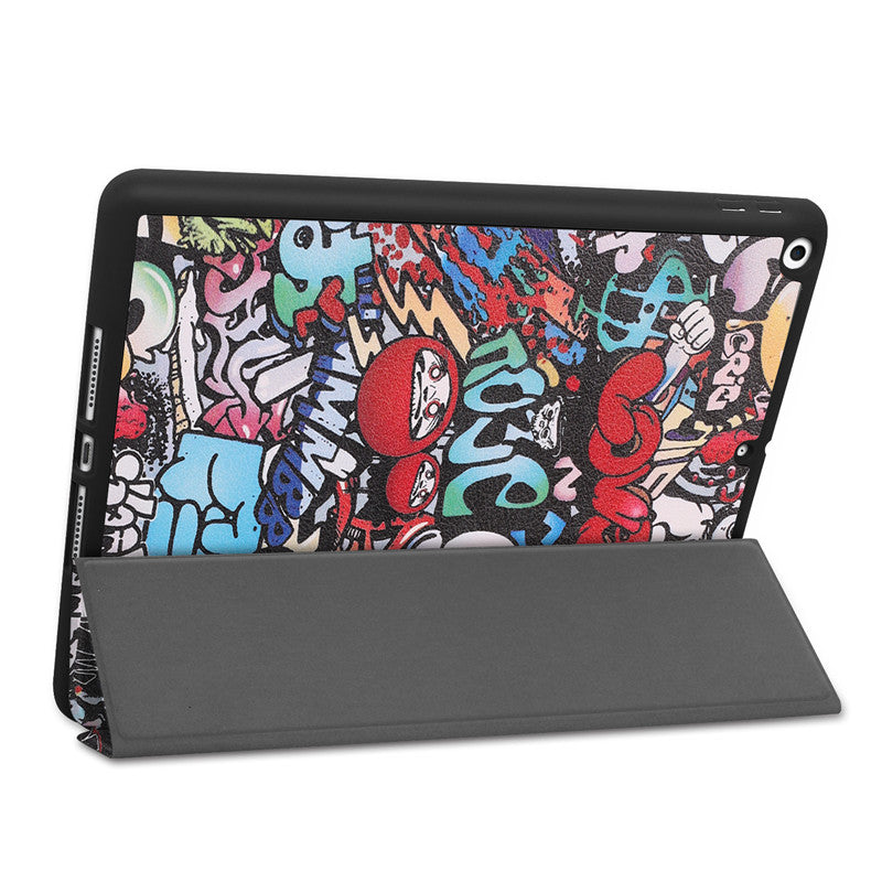 Das ArktisPRO iPad 10,2" PREMIUM SmartCase von ArktisPRO besticht durch ein lebendiges Design im Graffiti-Stil mit Cartoonfiguren, fettem Text und einem Halter für den Apple Pencil. Es steht aufrecht, wobei die Hülle als Ständer eingeklappt ist.
