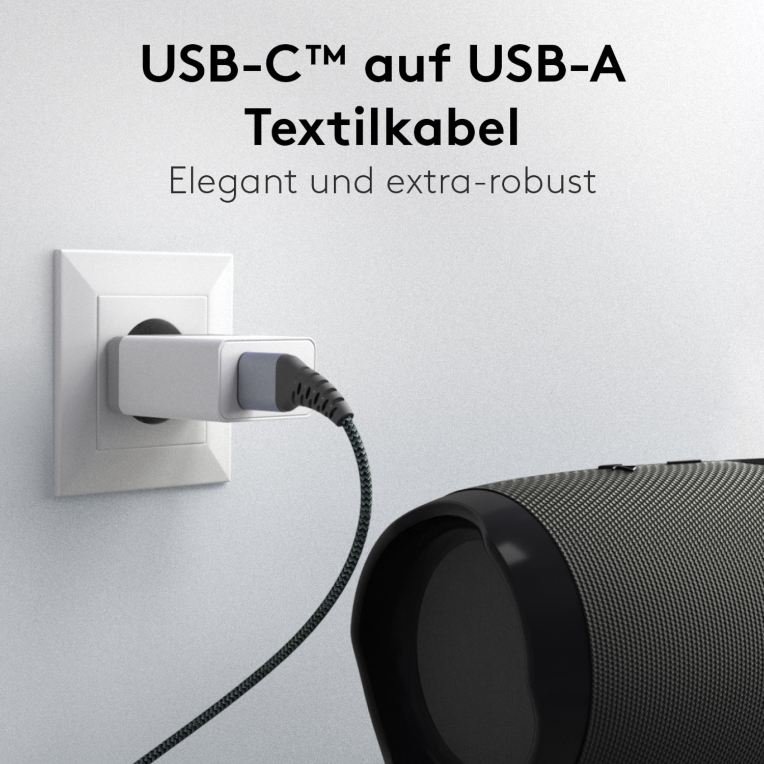Ein geflochtenes Goobay USB-C auf USB-C Textilkabel mit Metallsteckern wird in einen Wandadapter gesteckt und mit einem schwarzen Lautsprecher verbunden. Der Satz „USB-C auf USB-C Textilkabel Elegant und extra-robust“ hebt schnelle Datenübertragung oben hervor.