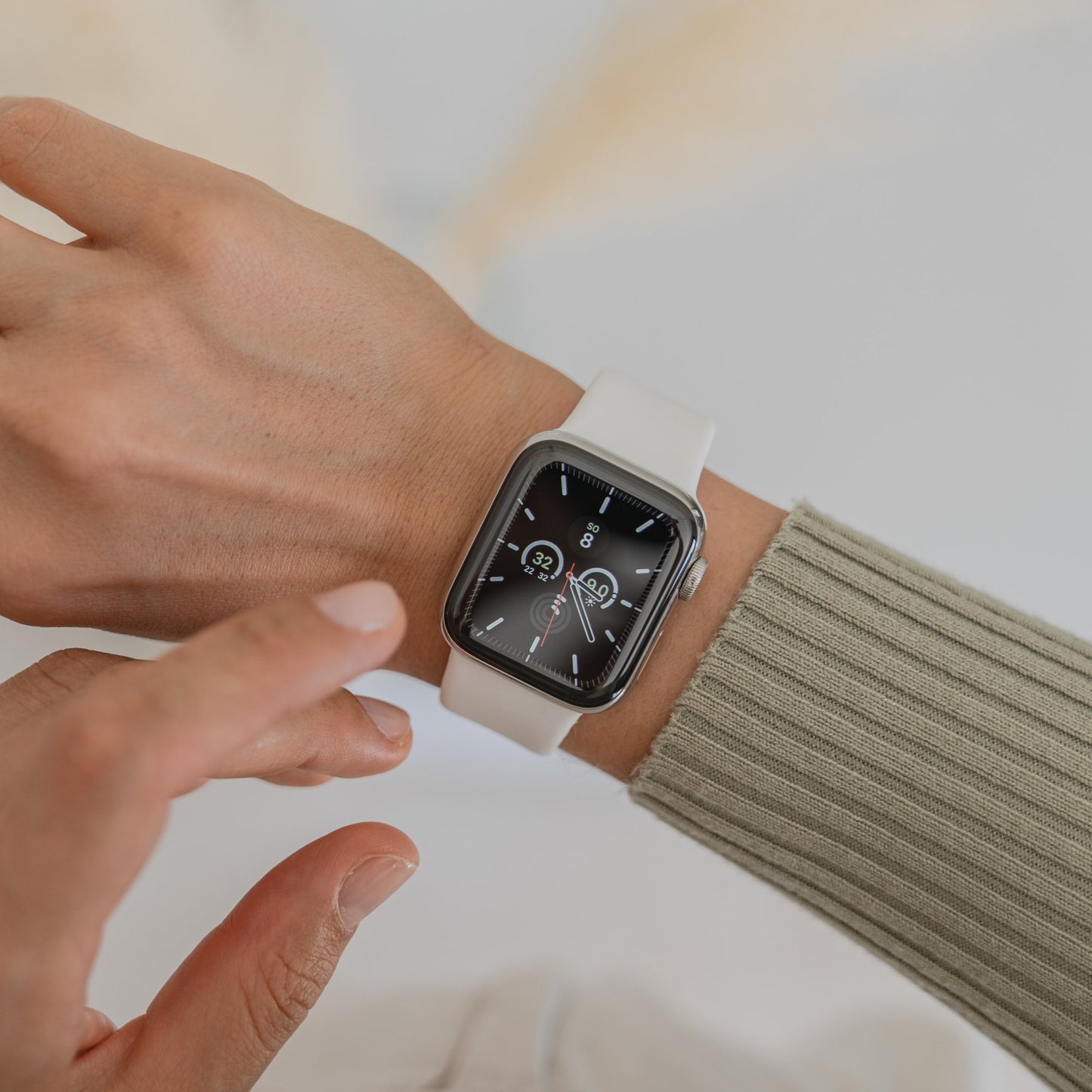 Eine Person trägt ein Arktisband Apple Watch Silikonarmband „Aqua“ mit einem schwarzen Display, das Zeit und Gesundheitsstatistiken anzeigt, berührt das Zifferblatt und trägt ein hellgrünes geripptes Langarmshirt.