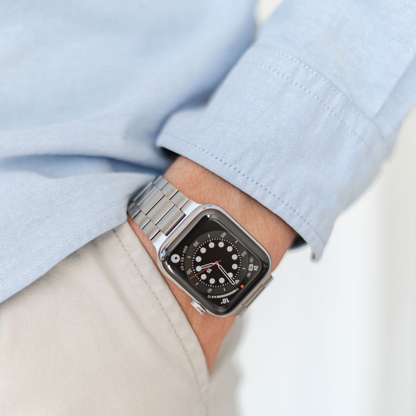 Eine Person in einem hellblauen Langarmshirt und einer beigen Hose hat die linke Hand in der Tasche und präsentiert ein arktisband Apple Watch Edelstahl Gliederarmband „Edition S“ mit minimalistischem Design am Handgelenk.