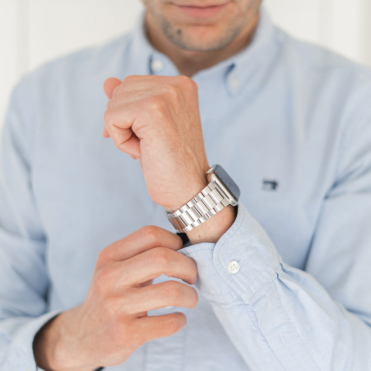 Eine Person in einem hellblauen Hemd richtet ihre Manschette und trägt am anderen Handgelenk ein arktisband Apple Watch Edelstahl Gliederarmband „Edition S“. Ihr Gesicht ist teilweise sichtbar, was das minimalistische Design von arktisband unterstreicht.