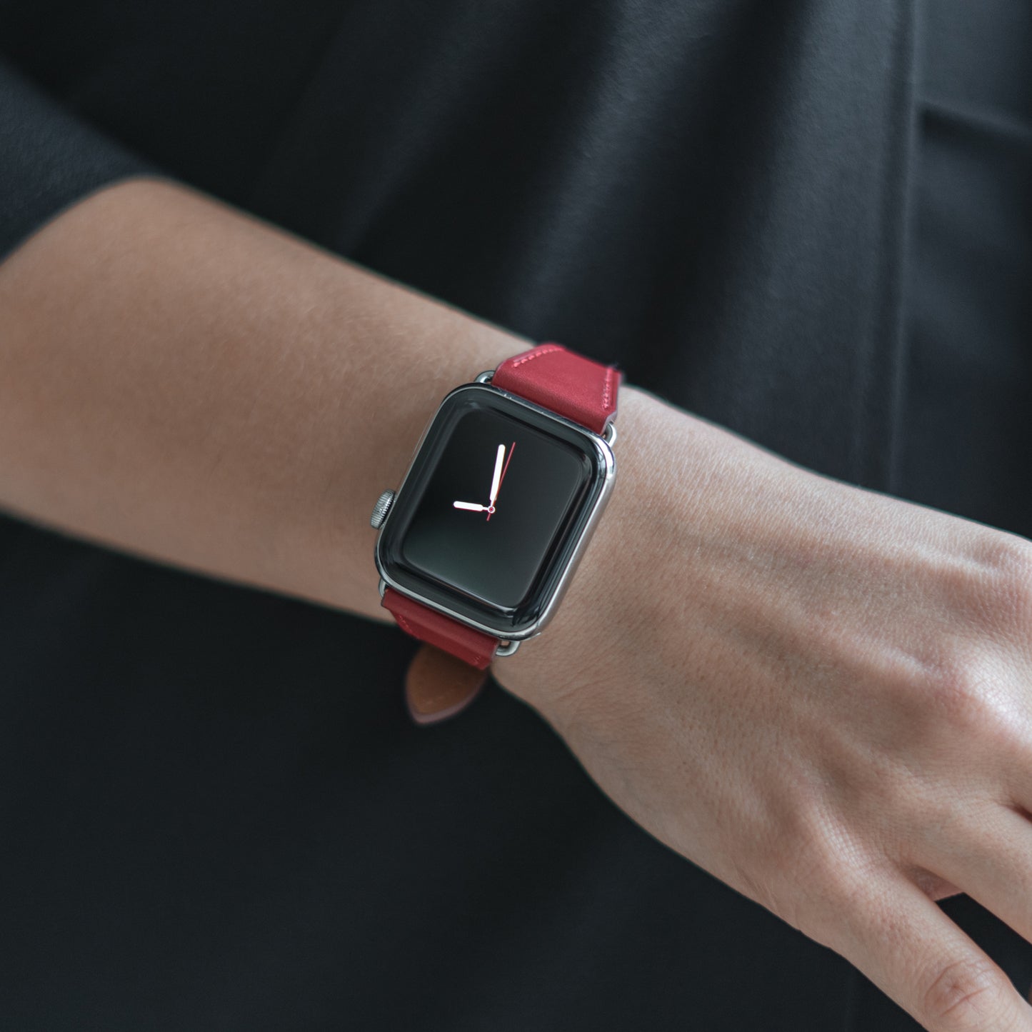 Eine Person in dunkler Kleidung trägt ein arktisband Apple Watch Lederarmband „Napoli“ von arktisband. Die Smartwatch zeigt eine analoge Uhr mit minimalistischen Stunden- und Minutenzeigern.