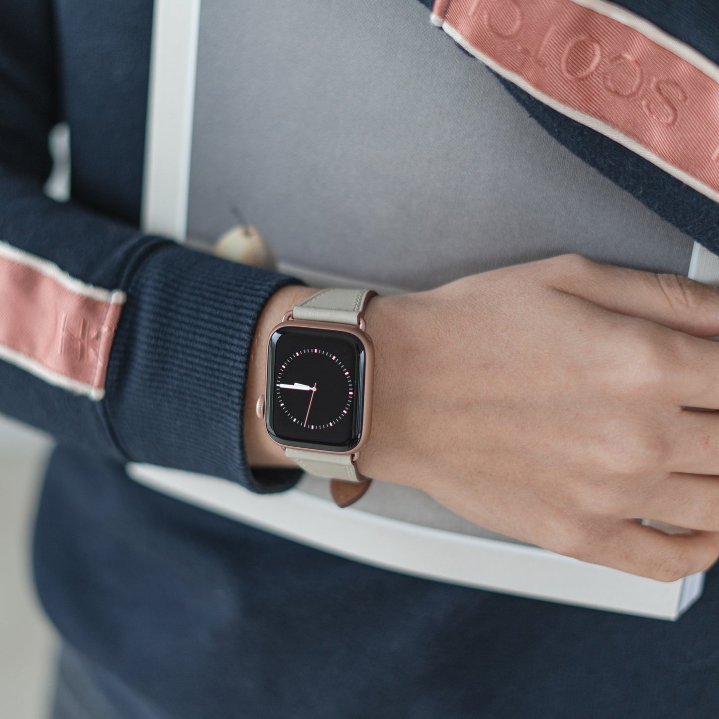 Eine Person in einer dunkelblau-pinken Jacke hält einen zugeklappten Laptop vor der Brust. Am Handgelenk trägt sie das arktisband Apple Watch Lederarmband „Napoli“ von arktisband, das mit seinem analogen Zifferblatt für minimalistischen Stil sorgt.