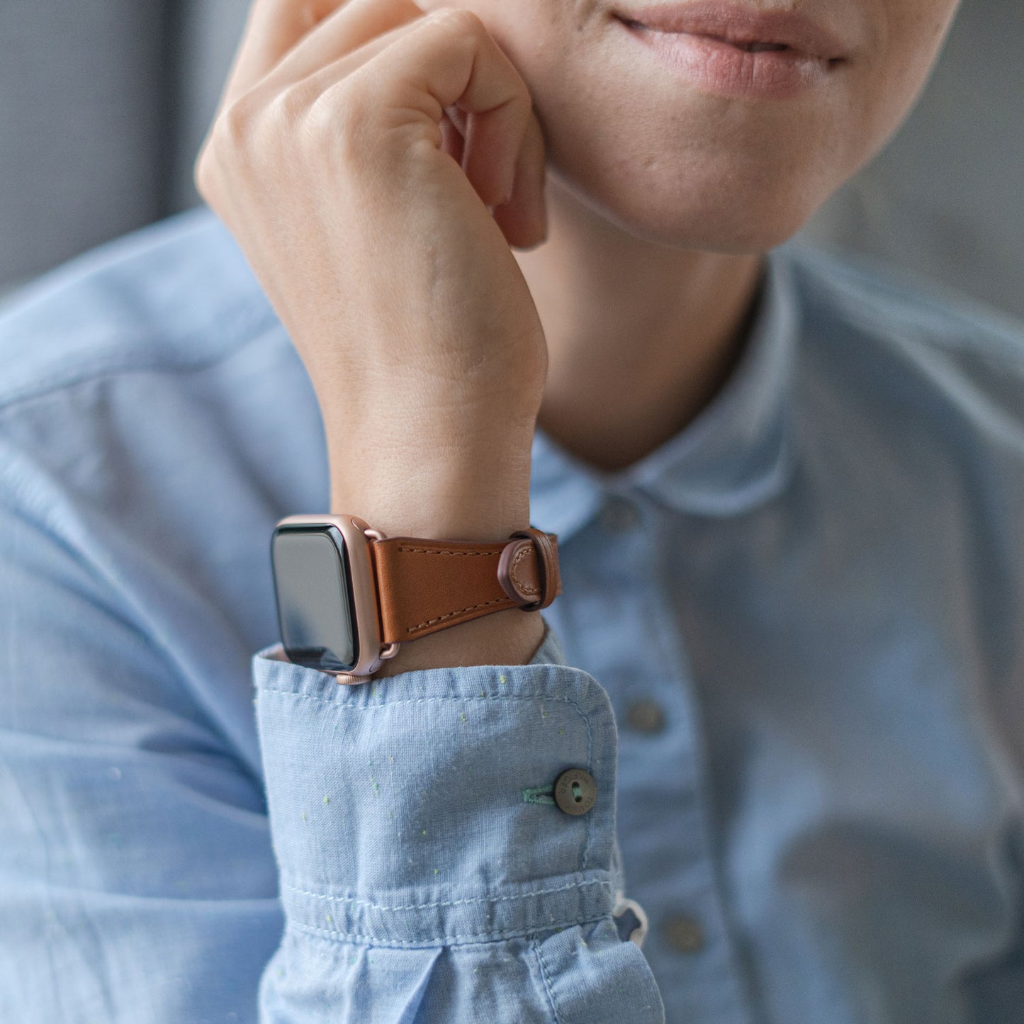 Eine Person in einem hellblauen Hemd stützt ihr Kinn auf die Hand und präsentiert das arktisband Apple Watch Lederarmband „Napoli“ in Braun. Der minimalistische Stil wird durch das leere Zifferblatt betont.