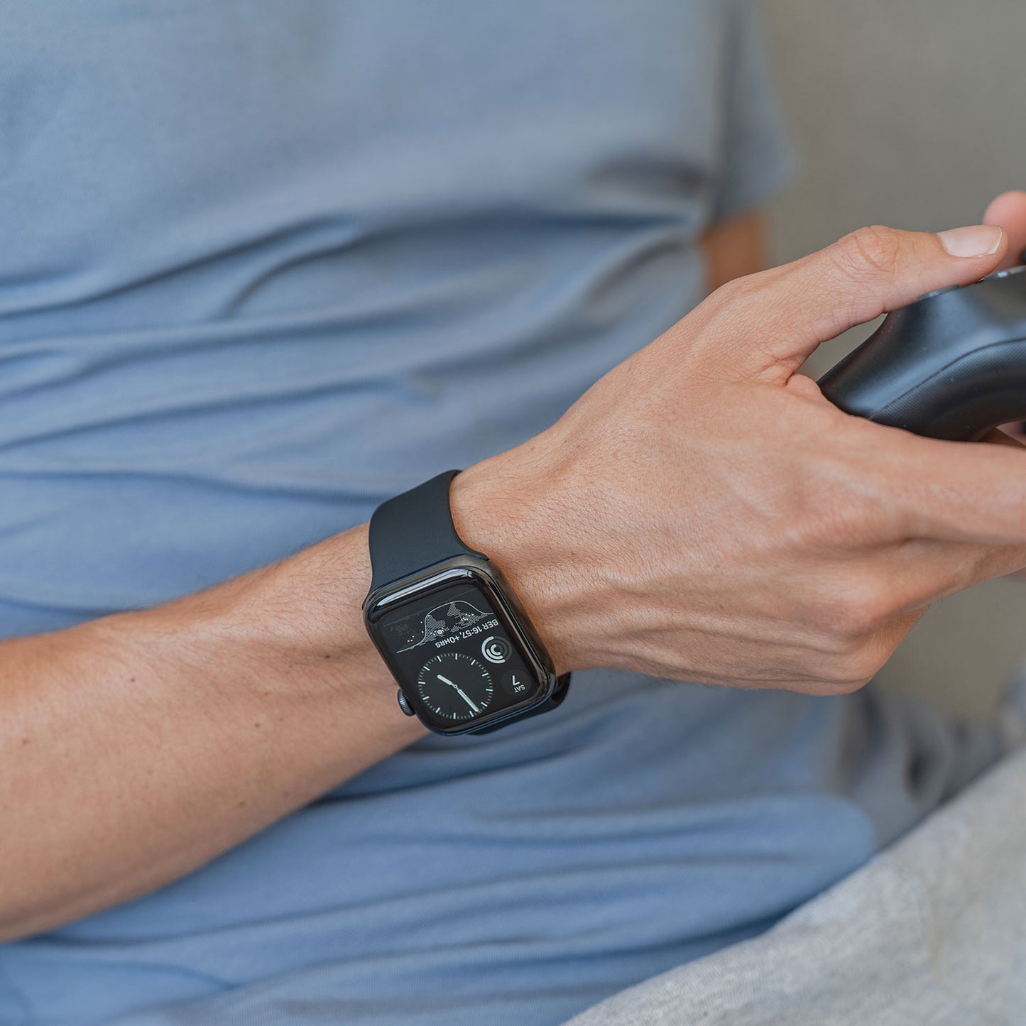 Eine Person trägt das Arktisband Apple Watch Silikonarmband „Aqua“ und hält einen Gamecontroller in der Hand. Sie trägt ein hellblaues Hemd und eine hellgraue Hose.