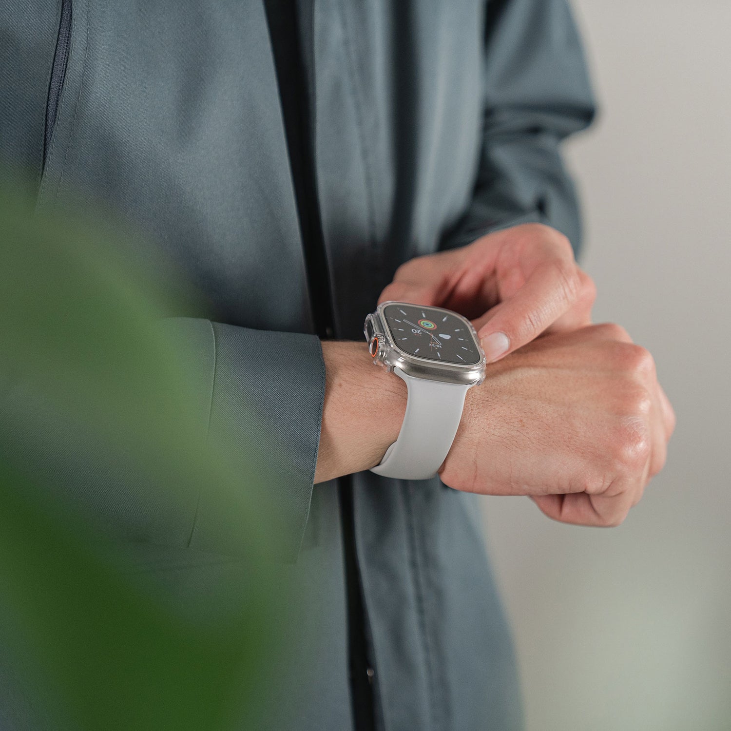 Eine Person in einem grauen Hemd richtet eine Apple Watch Ultra 49 mm mit weißem Armband, geschützt durch den ArktisPRO CRYZTAL BUMPER aus strapazierfähigem Polycarbonat-Material.