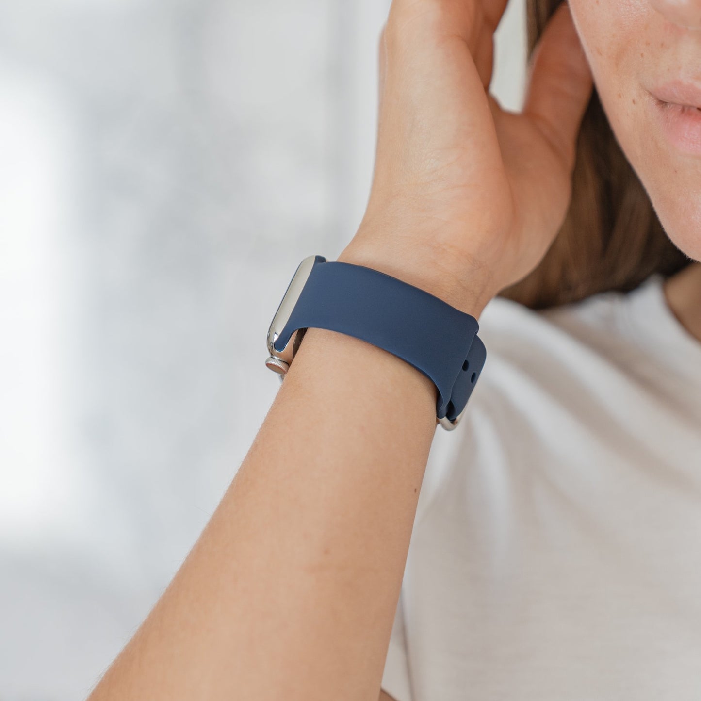 Eine Person im weißen Hemd ist in Nahaufnahme zu sehen. Sie trägt das arktisband Apple Watch Silikonarmband „Aqua“ von arktisband am Handgelenk. Ihre Hand befindet sich in der Nähe ihres Ohrs vor einem hellen, unscharfen Hintergrund.