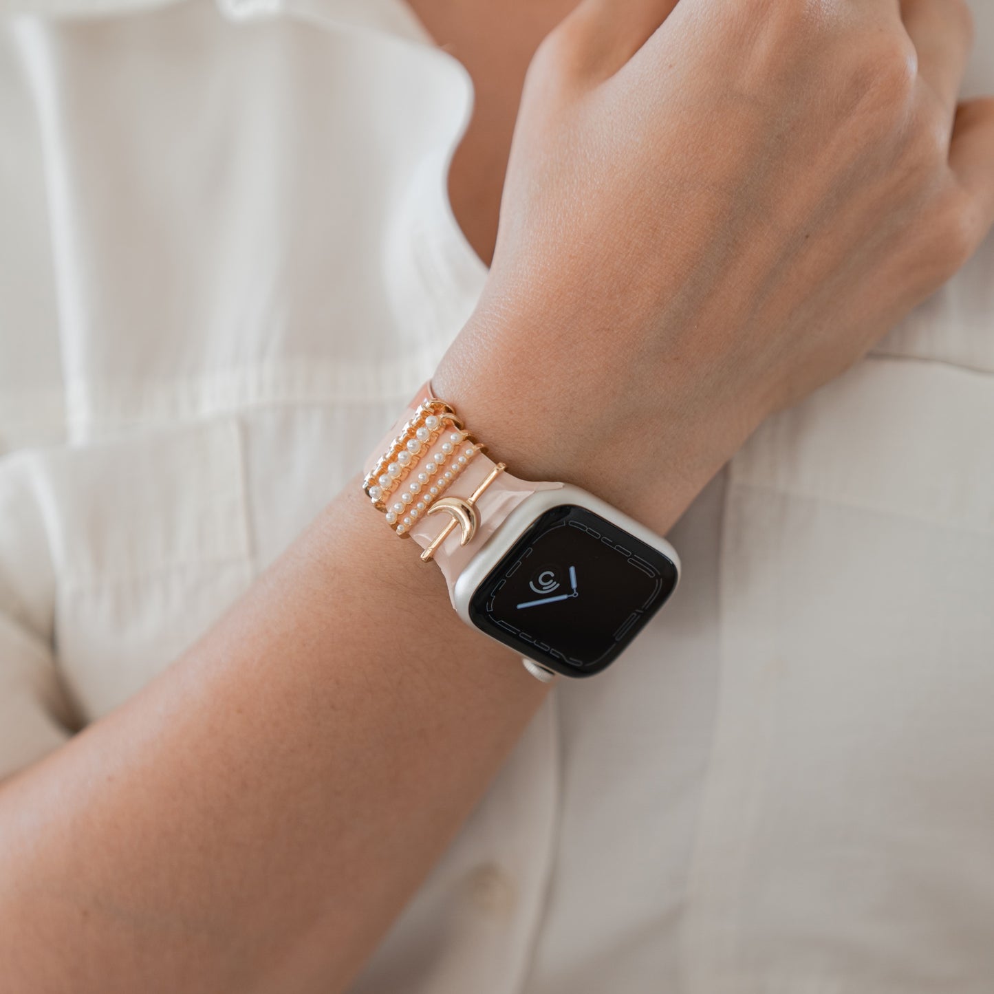 Eine Person in einem weißen Hemd präsentiert ihr linkes Handgelenk mit einem arktisband Apple Watch Armband Charm aus Perlen und Goldperlen. Die Uhr zeigt 9:00 Uhr und unterstreicht den individuell gestaltbaren Stil von arktisband.