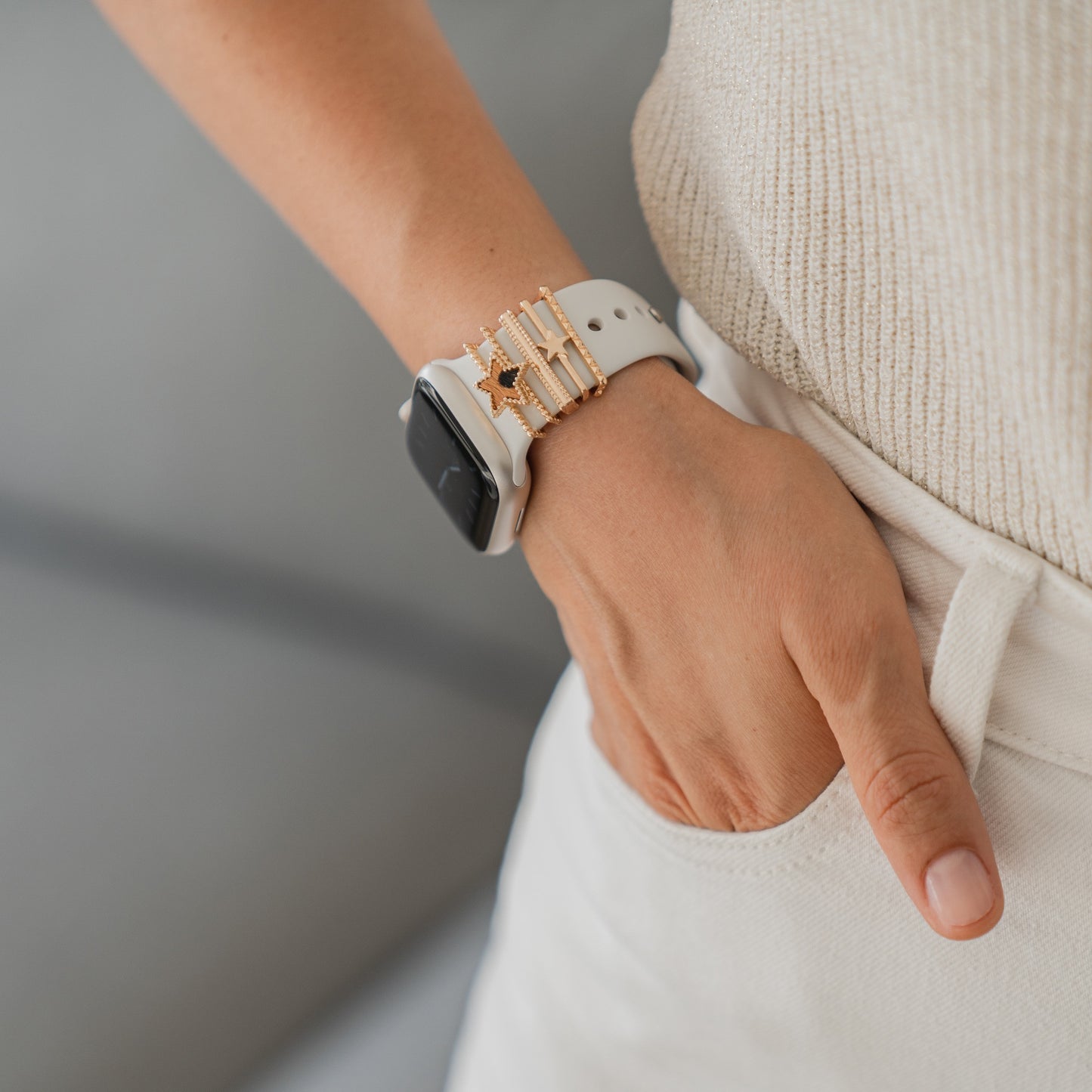 Jemand in cremefarbener Hose hat die Hand in der Tasche und präsentiert arktisband Apple Watch Armband Charms von arktisband mit weißen und goldenen Akzenten. Der sanft verschwommene Hintergrund unterstreicht die Optik des Accessoires.