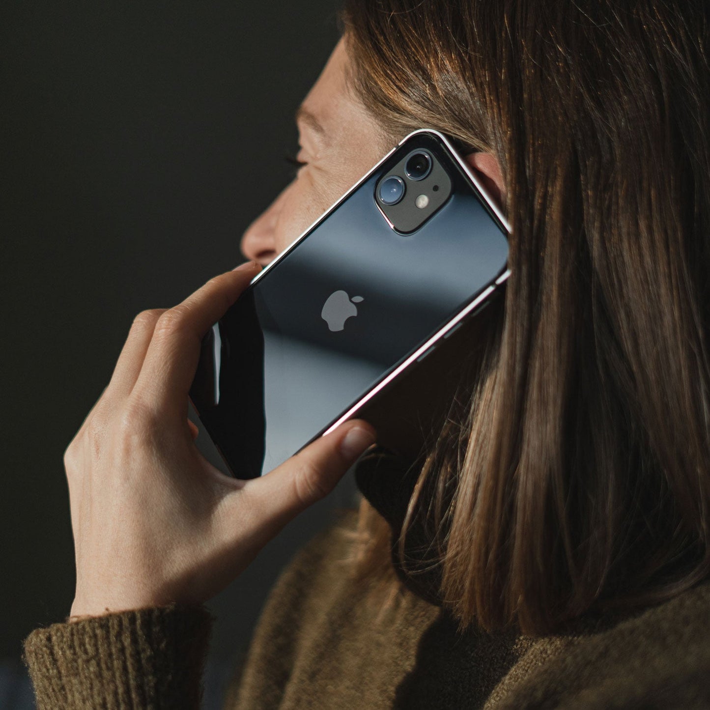 Eine Person telefoniert und hält vor einem dunklen Hintergrund ein schwarzes iPhone mit einem Aviato AirZERO Alu Bumper für iPhone 14 von Aviato.