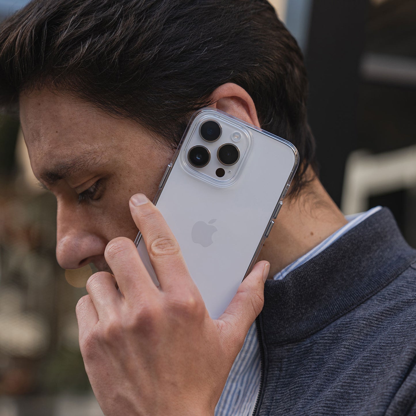 Eine Person in einer grauen Jacke hält im Freien ein iPhone 14 Pro Max mit einer MR PROTECT CLEAR Hülle ans Ohr und telefoniert. Die MR PROTECT Hülle ist transparent und zeigt die drei Kameralinsen des Telefons.