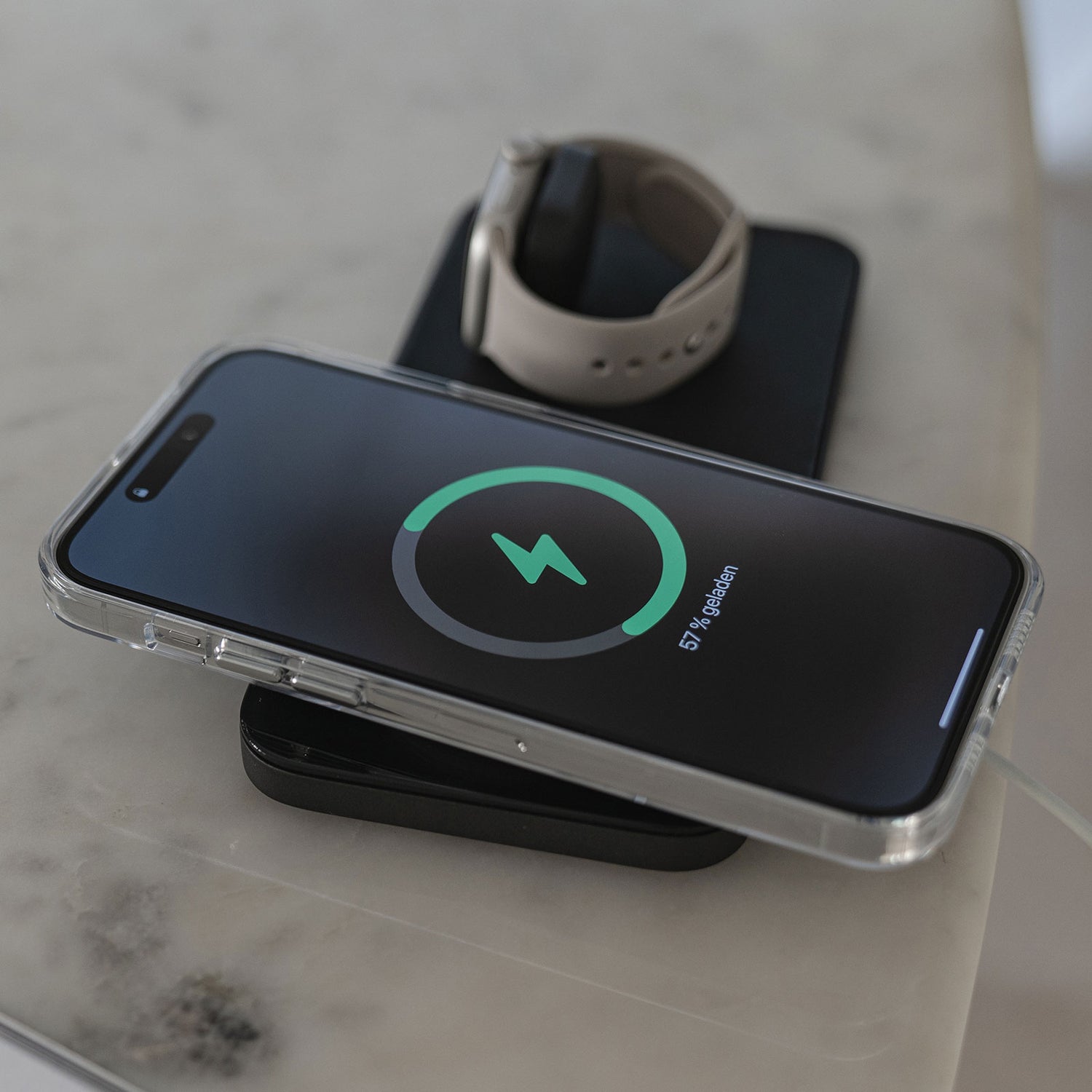 Ein iPhone 14 Pro in der transparenten MR PROTECT iPhone 14 Pro CLEAR Case mit MagSafe von MR PROTECT zeigt den Ladebildschirm und liegt auf einem kabellosen Ladepad neben einer Smartwatch auf Marmor.