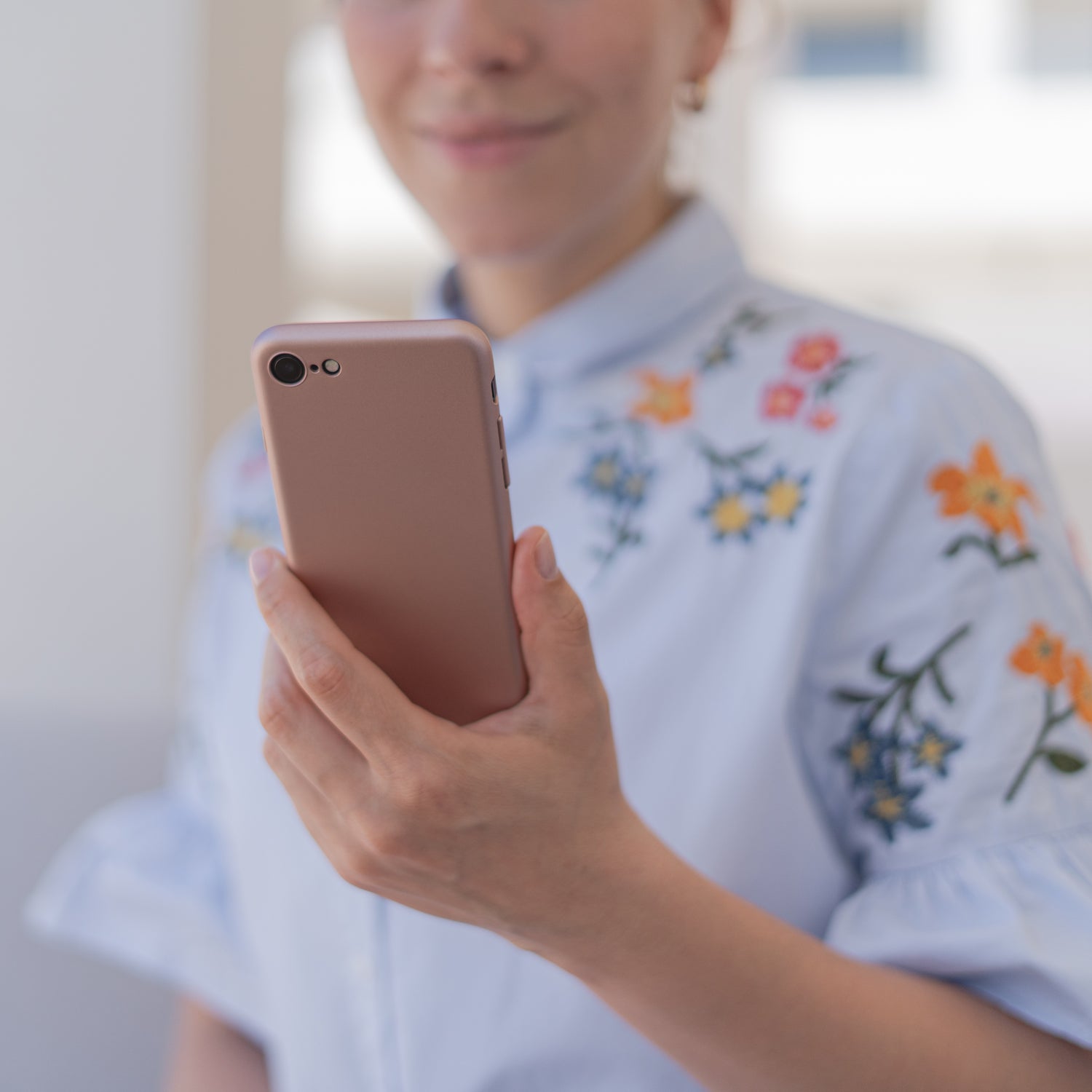 Eine Frau in einem hellblauen Blumenhemd hält ein roségoldenes iPhone 8 mit dem ArktisPRO iPhone 8 UltraSlim Hardcase und blickt auf den Bildschirm.