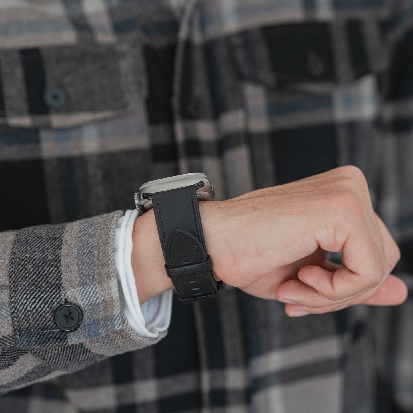Eine Person trägt ein Mobiletto Apple Watch Ultra Lederarmband von Mobiletto mit einer Apple Watch Ultra über einem karierten Hemdärmel.