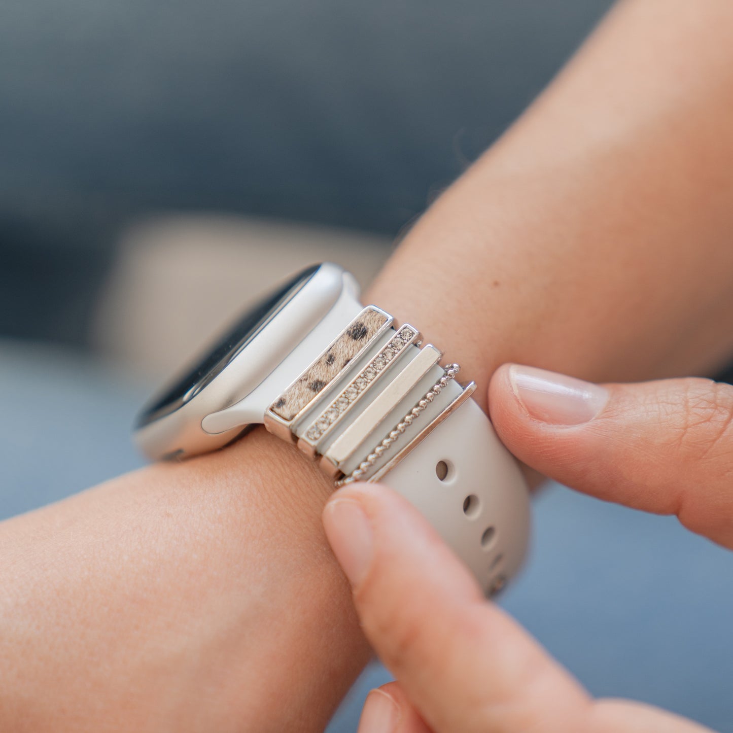 Eine Person passt ein leichtes Arktisband-Smartwatch-Armband an, das mit mehreren dünnen Armbändern und Arktisband-Apple-Watch-Armband-Charms für einen einzigartigen, anpassbaren Look gestylt ist.