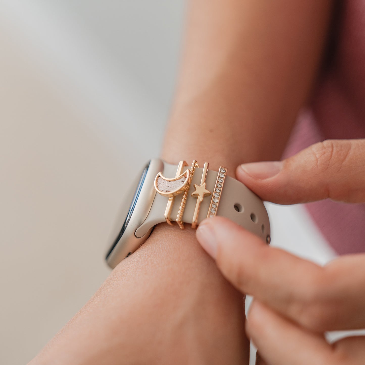 Eine Nahaufnahme zeigt ein Handgelenk mit einem Arktisband Apple Watch Armband Charms Set von Arktisband auf einem beigen Armband mit goldenen Mond-, Balken- und Sternanhängern. Eine Hand passt die anpassbaren Anhänger am Armband an.
