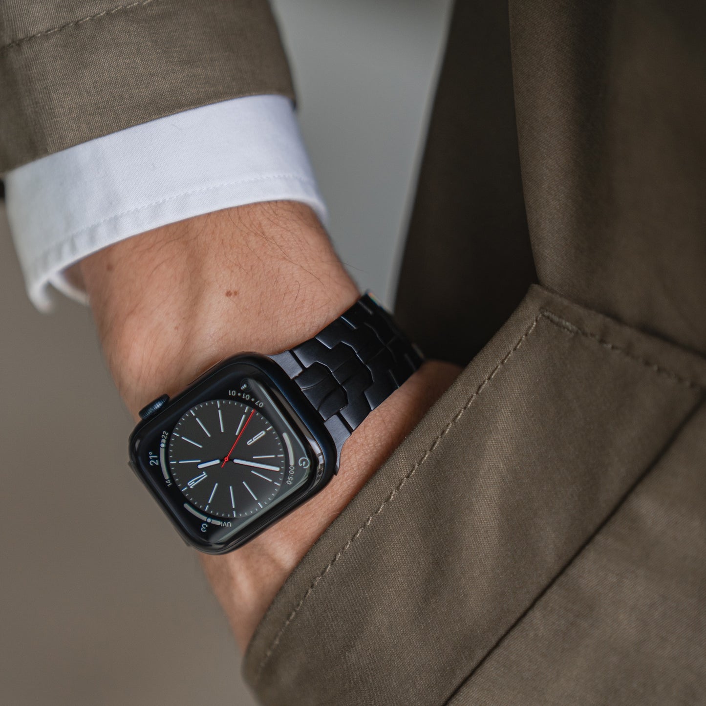 Jemand, der ein arktisband Apple Watch Edelstahlarmband „Momento“ von arktisband mit analogem Display trägt, hat seine Hand in der Tasche eines taupefarbenen oder braunen Mantels, unter dem Ärmel ist eine weiße Hemdmanschette sichtbar.