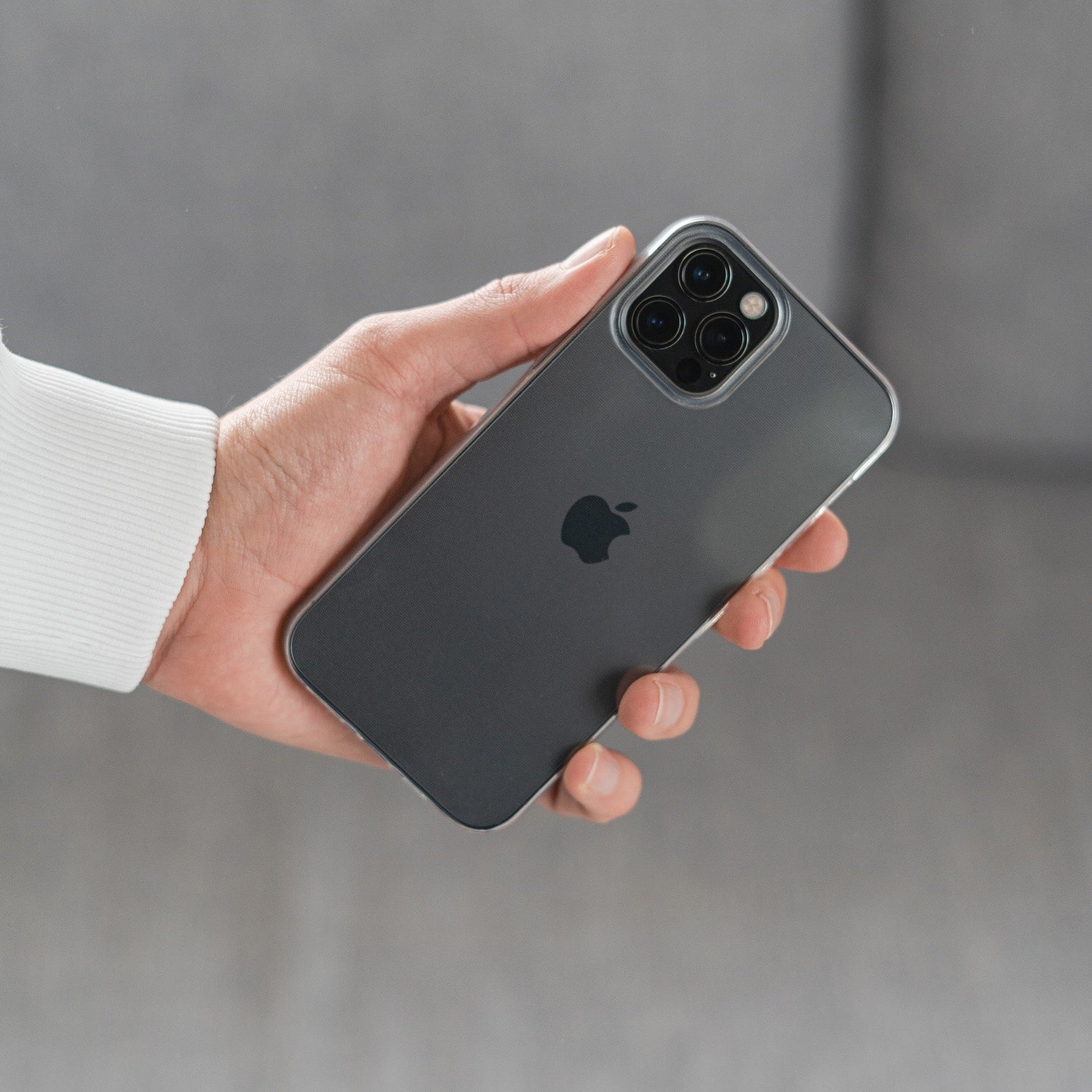 Eine Person hält ein schwarzes iPhone 14 Pro Max mit Dreifachkameras in einem ArktisPRO ZERO Case Ultra Clear (dünnste TPU-Silikon-Hülle) vor einem unscharfen grauen Hintergrund.
