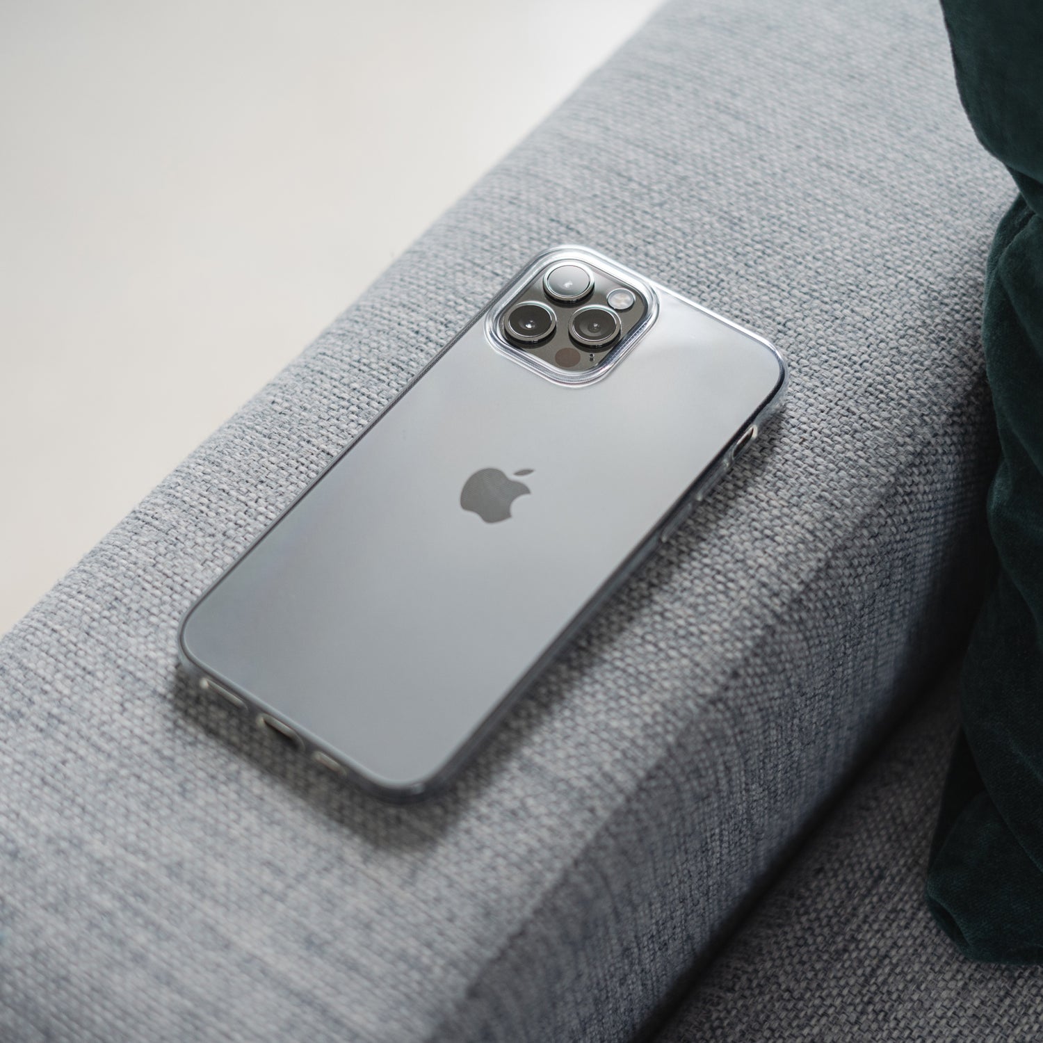 Ein silbernes iPhone 12 Pro Max mit dem ArktisPRO iPhone 12 Pro Max ZERO Case Ultra Clear von ArktisPRO liegt mit der Vorderseite nach unten auf einem hellgrauen Stoffsofa und zeigt das Apple-Logo und das Dreifachkameraobjektiv.